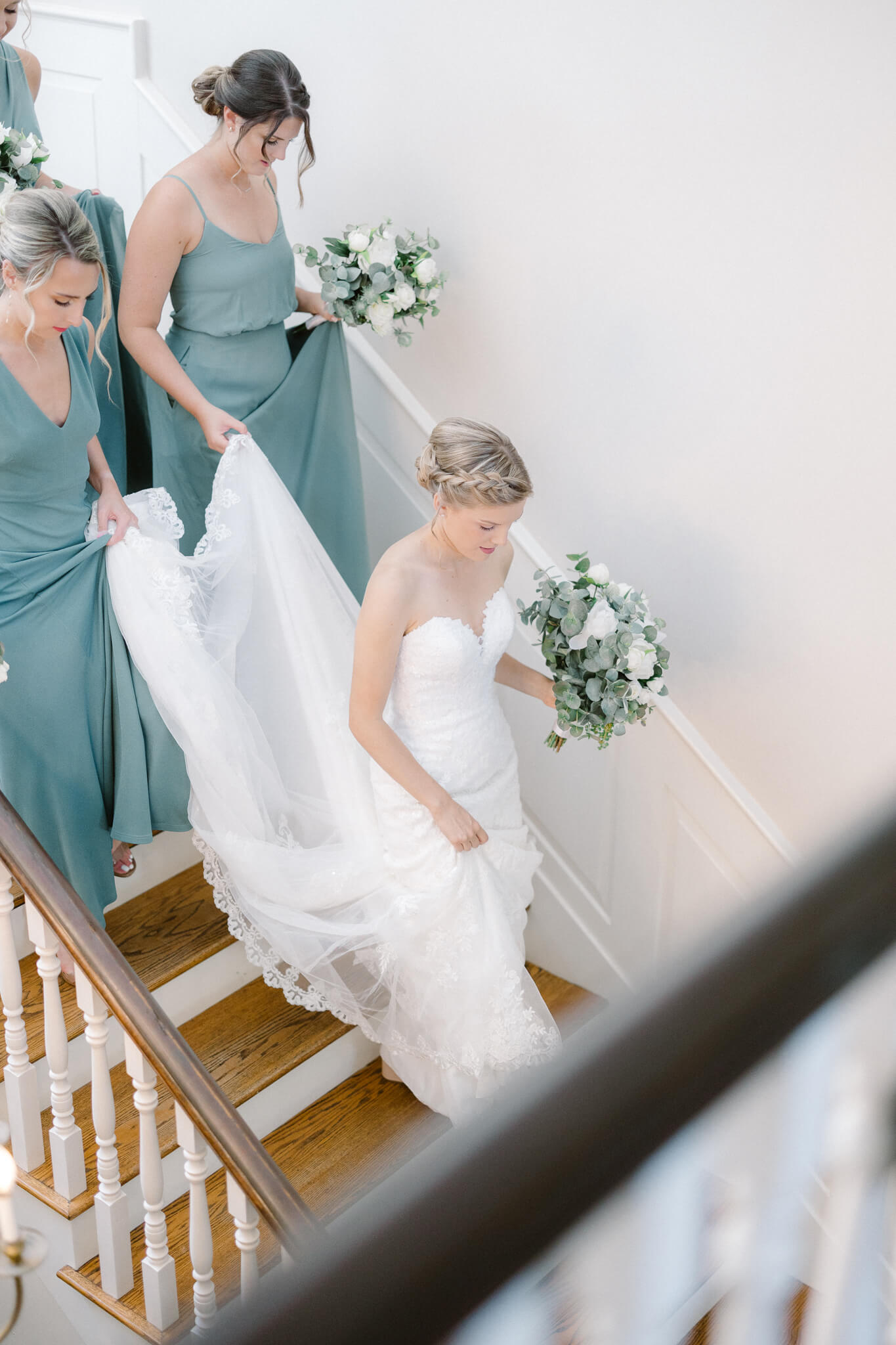 bridesmaids walking with bride down the stairs and carrying her train at Stone Manor Country Club