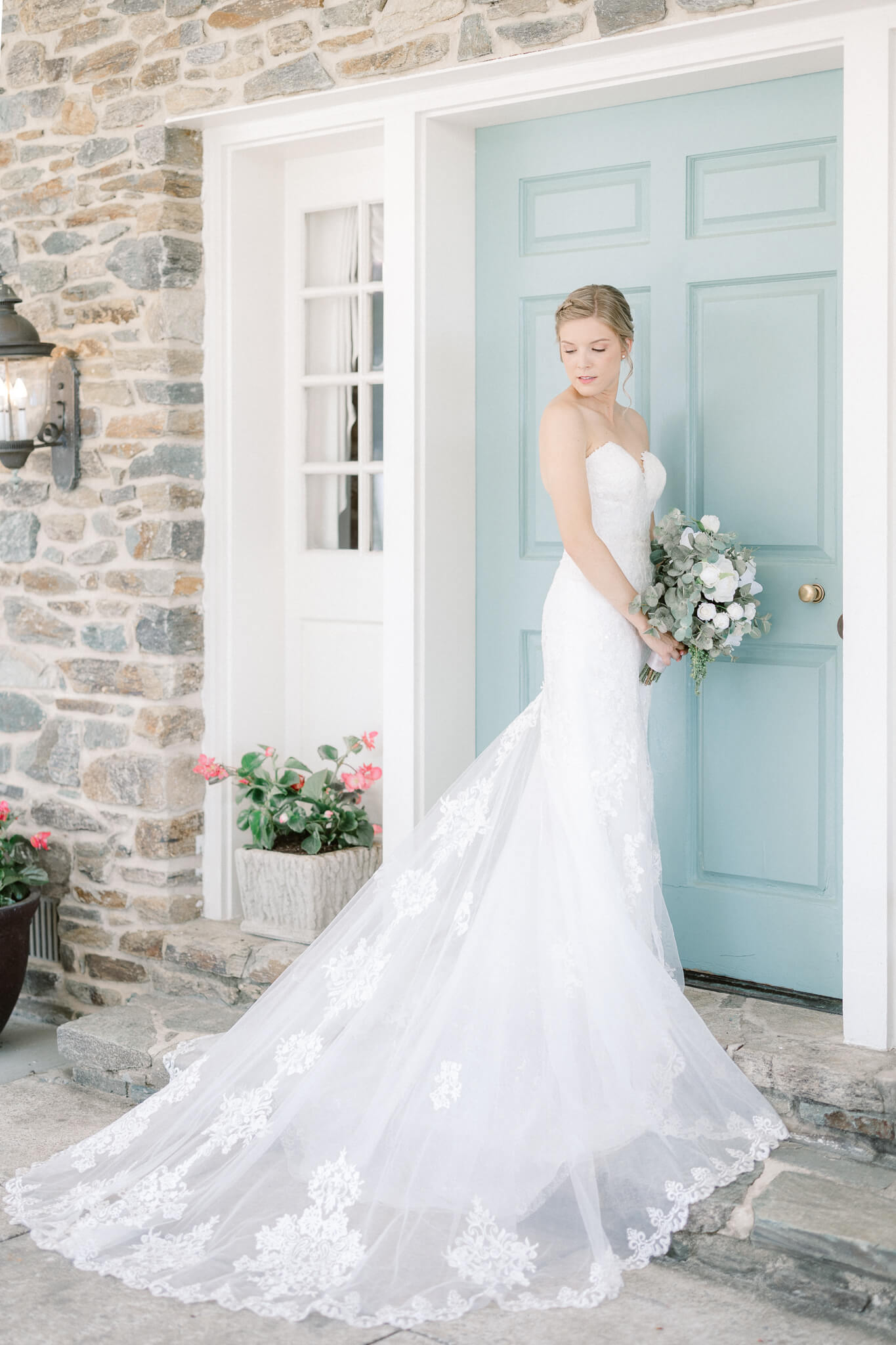 bride with fitted and long lace gown standing in front of a stone wall and blue door Stone Manor Country Club