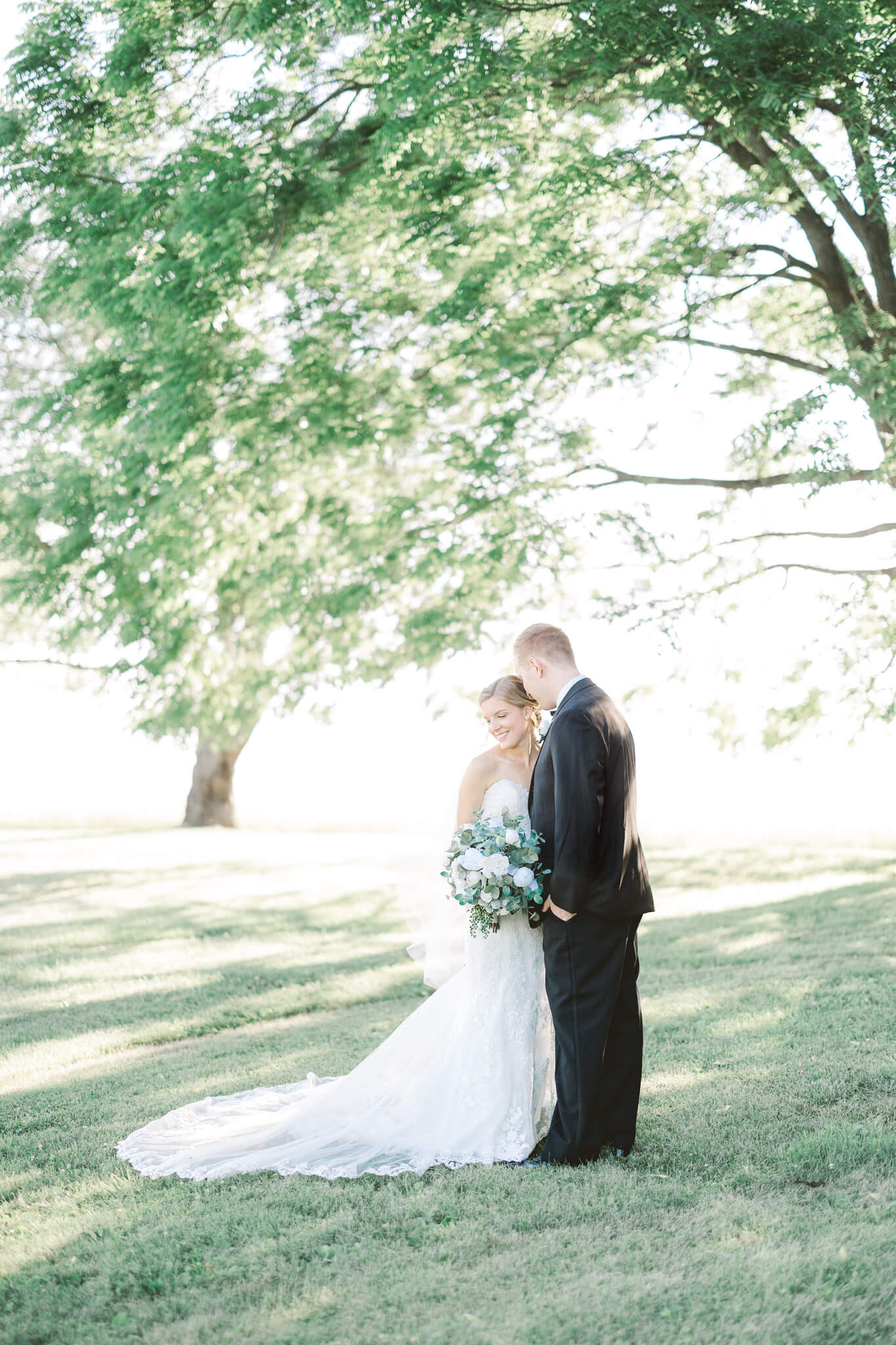 groom nuzzling with bride under a large tree