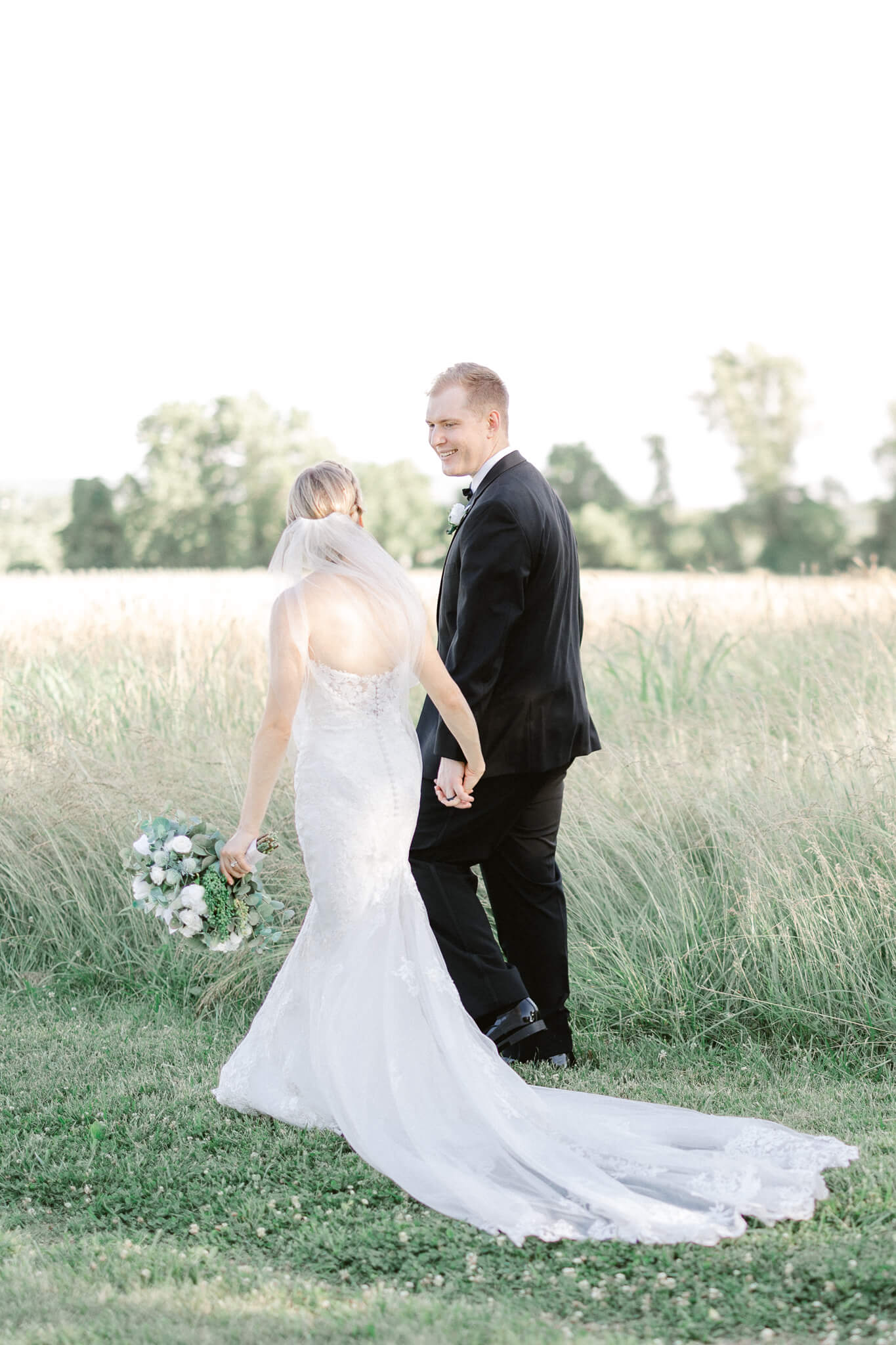 bride and groom walking hand in hand through a field Stone Manor Country Club