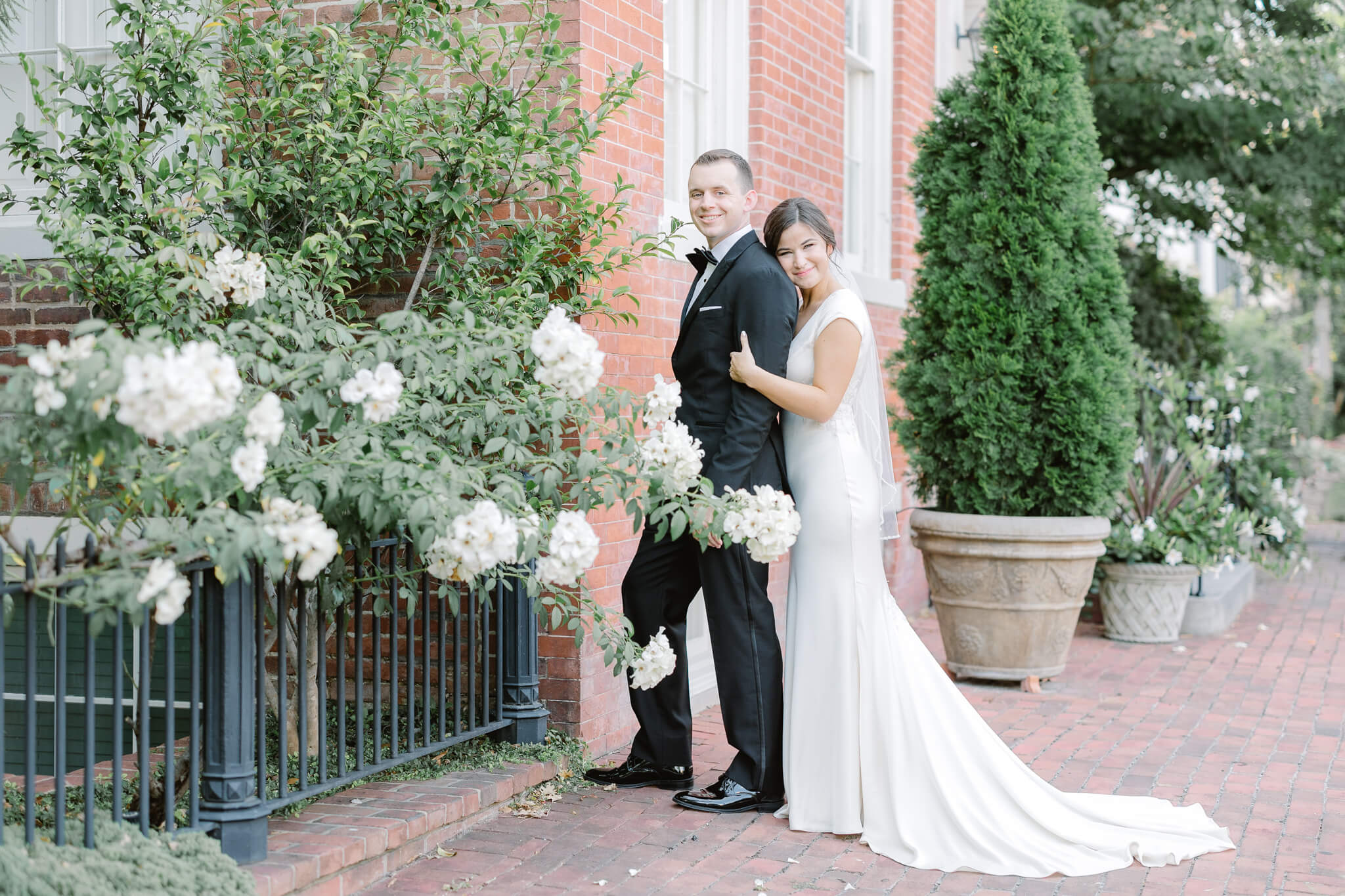 bride and groom hugging by white flowering bush at Old Town Alexandria Wedding