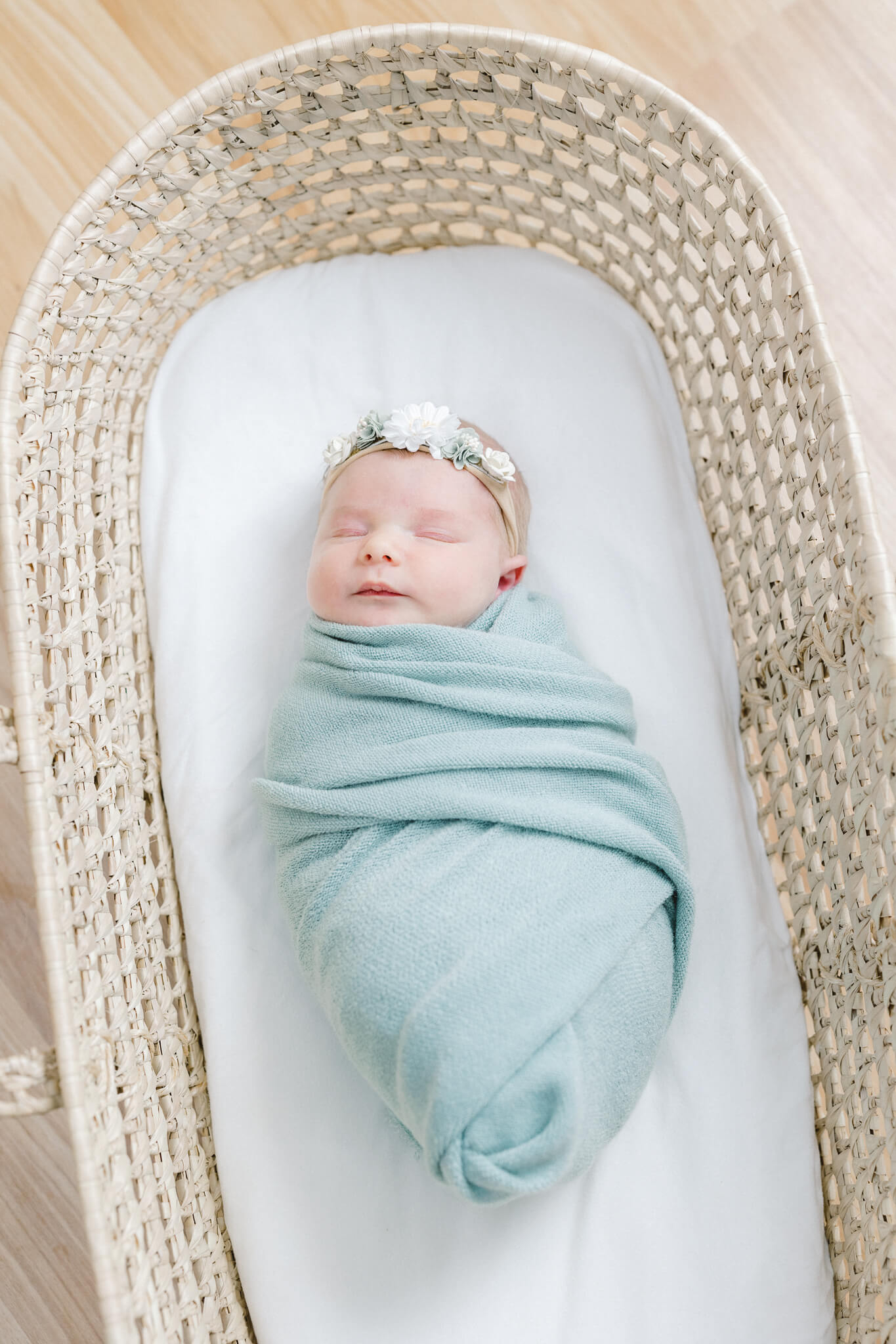 newborn baby wrapped in green wearing a flower headband and laying in a basket