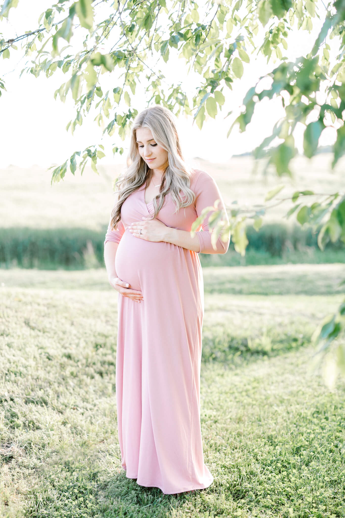 pregnant woman in pink dress looking down at her belly Southern Maryland Newborn Photographer