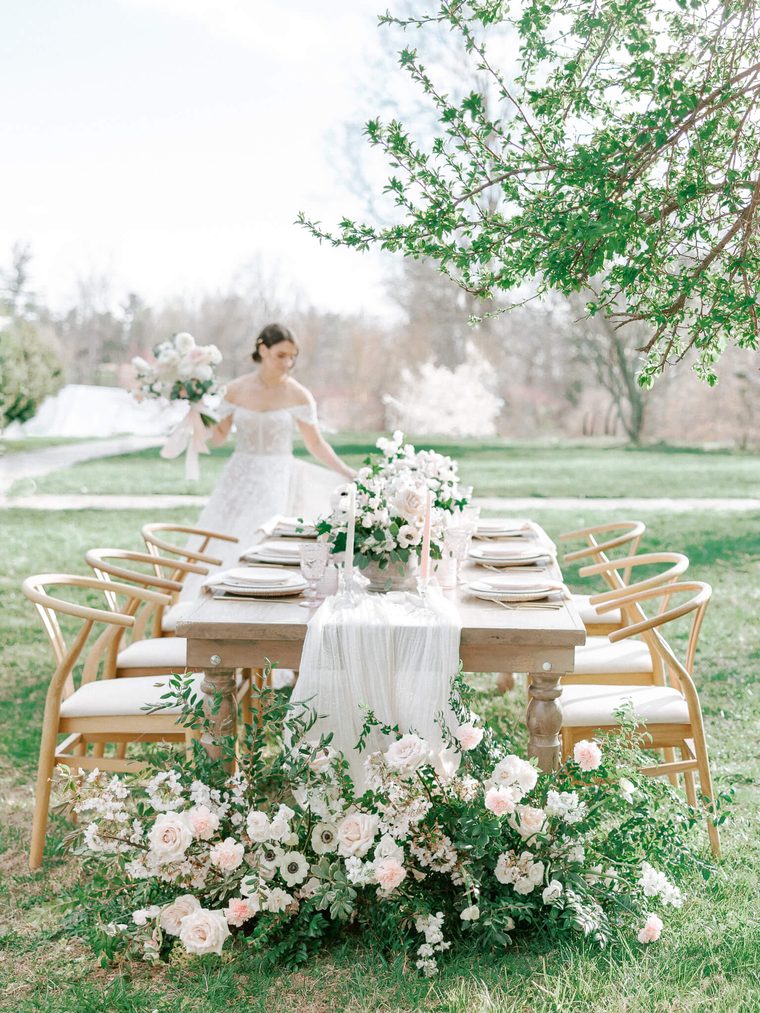 A bride admiring the table decor of blush, whites and greener at an outdoor reception.