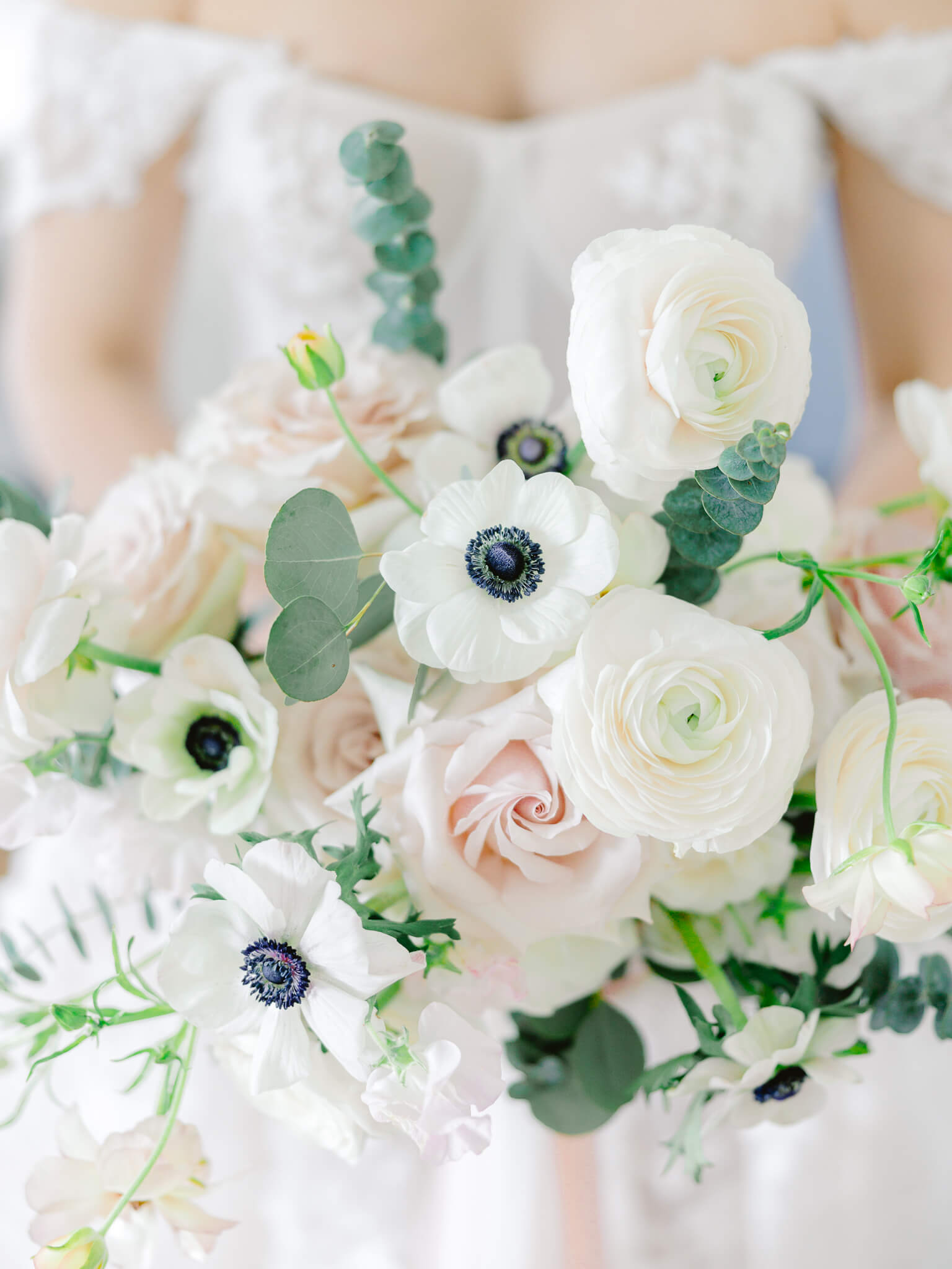 A close up of a bride in her wedding dress holding her bouquet of anemones, roses, eucalyptus and ranunculus.