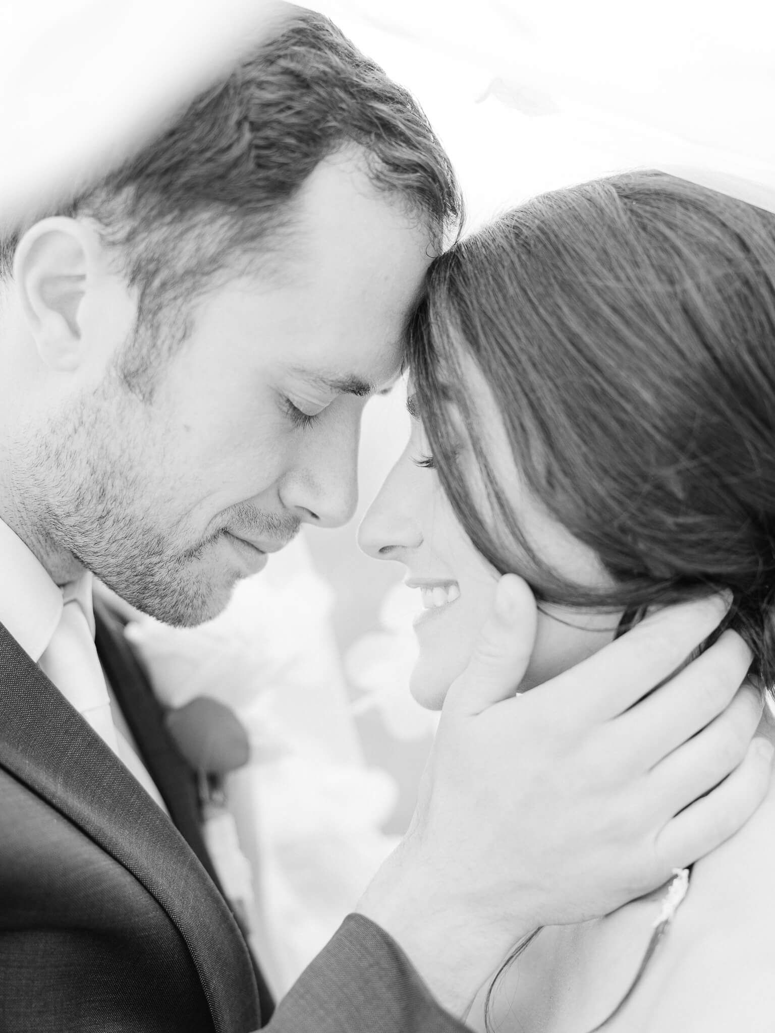 A black and white image of a groom resting his forehead against the bride's while holding her face in his hand.
