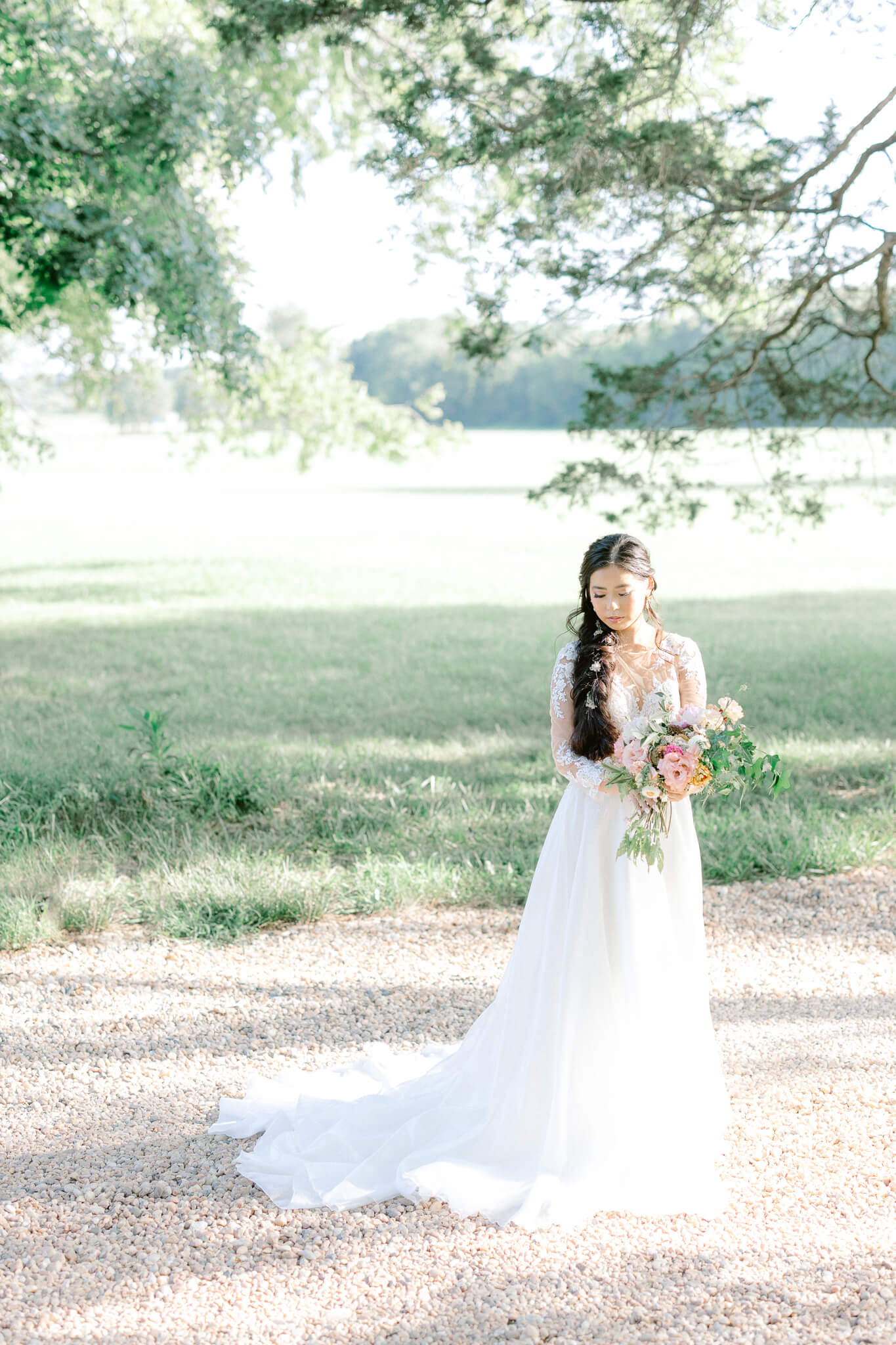 bride standing in field in wedding dress holding pink flowers