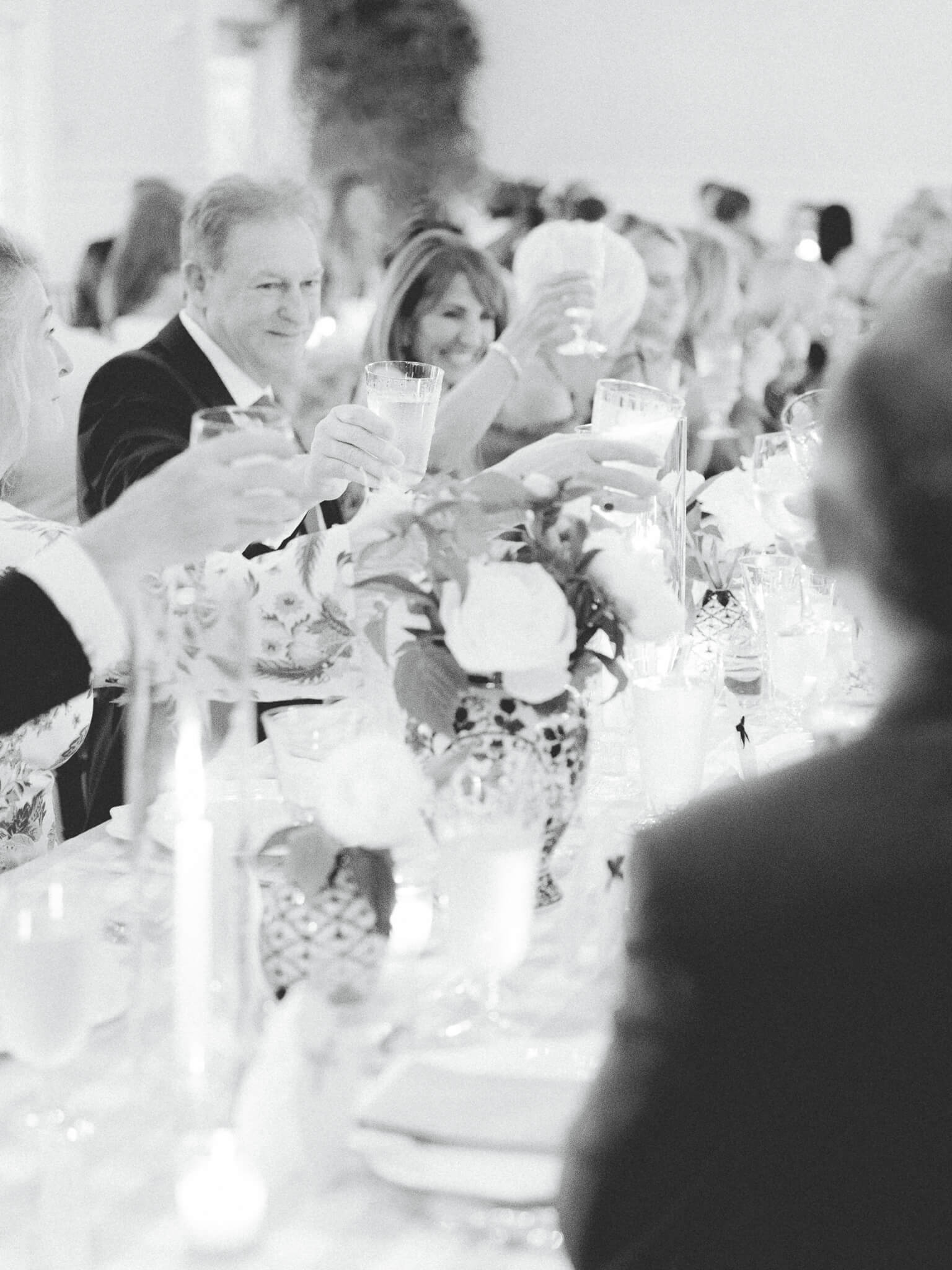 Black and white image of guests toasting during a candlelit wedding reception