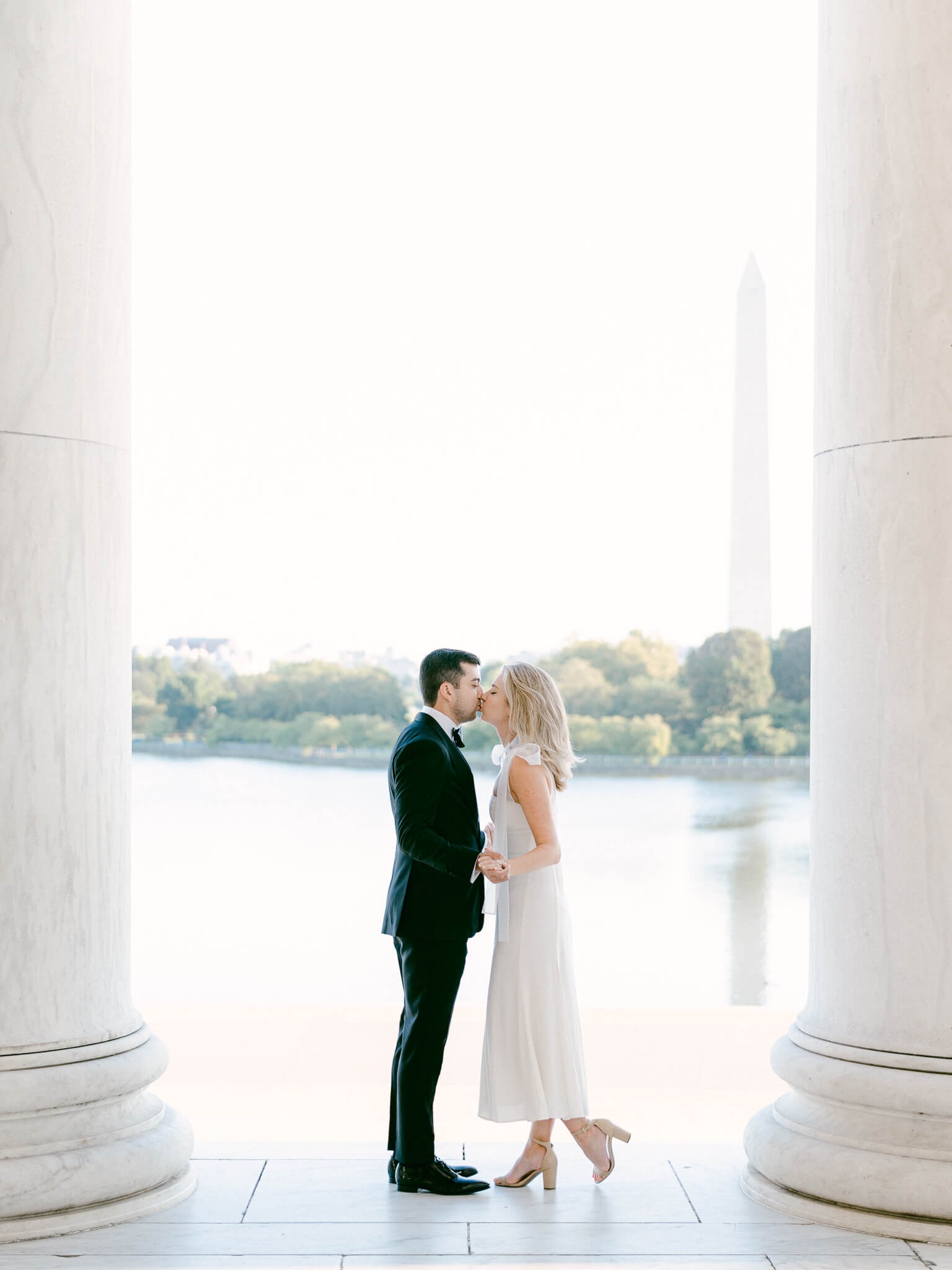 An engaged couple kissing between the columns of the Jefferson Memorial in Washington, D.C.