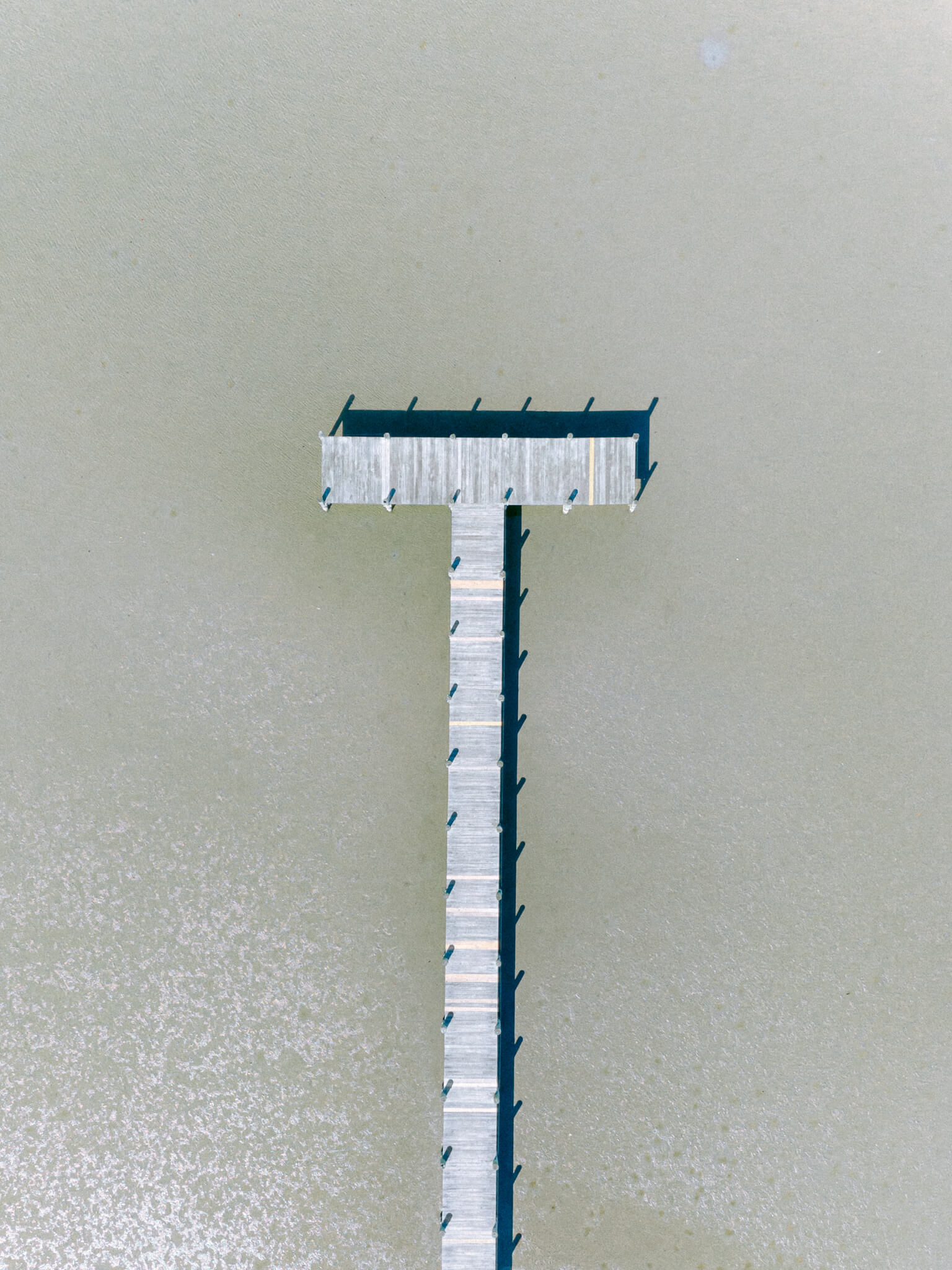 A t-shaped wooden dock in the water photographed from above
