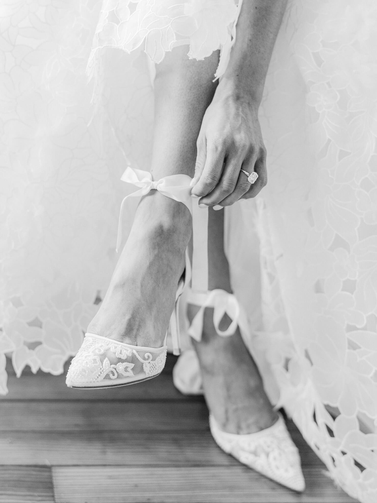 Close up of a bride's Bella Belle shoes as she is touching the tied bow on her foot.