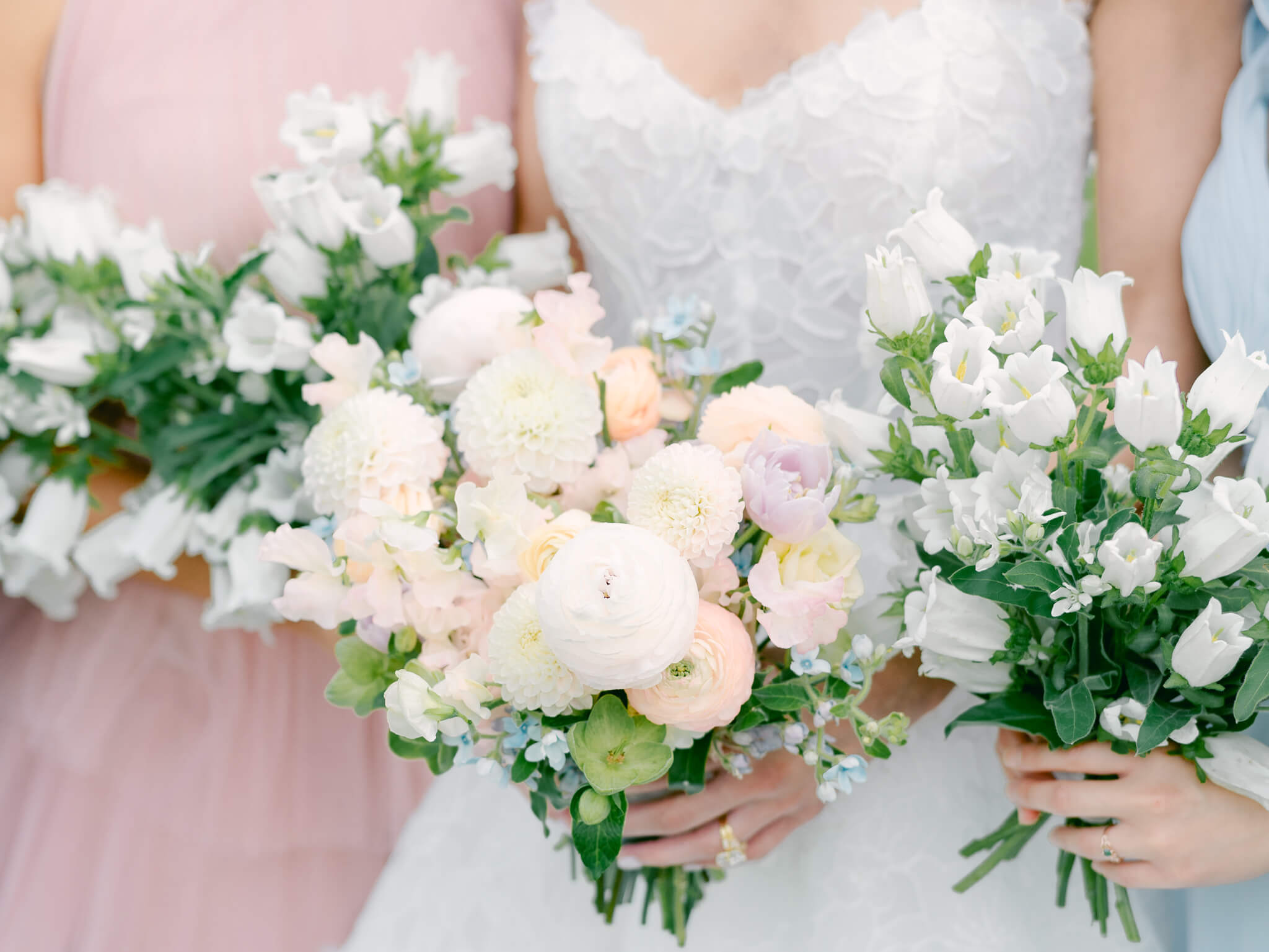 Closeup of the bride's and bridesmaids' pastel bouquets held in front of their white and blush gowns.