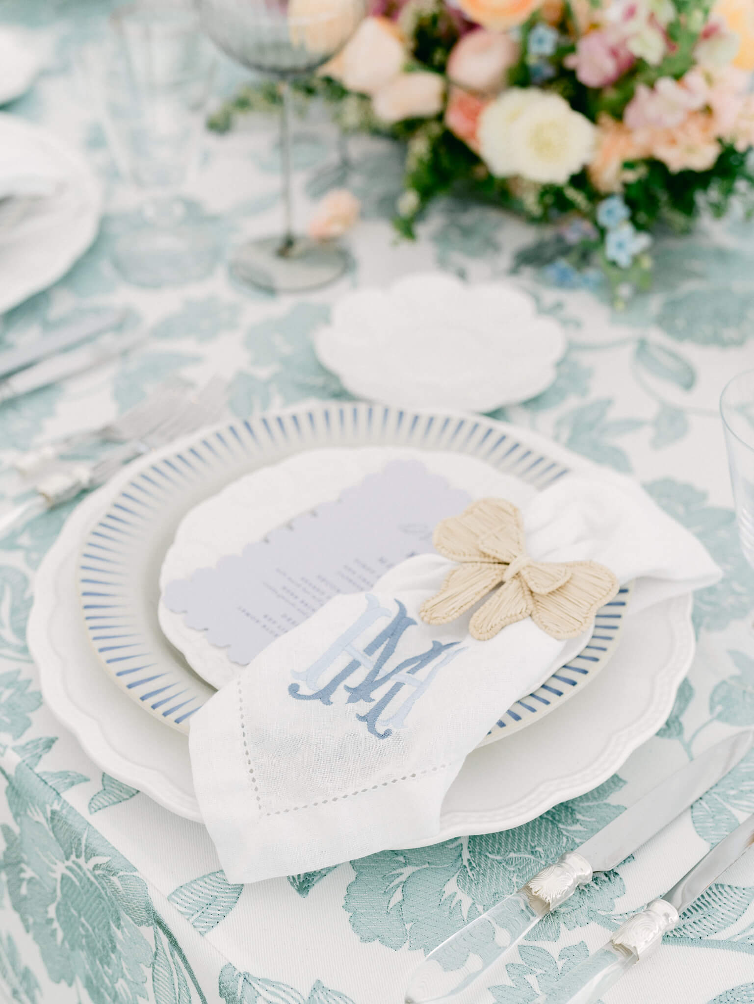 Closeup of a place setting with white and blue plates on a floral blue and white table cloth.