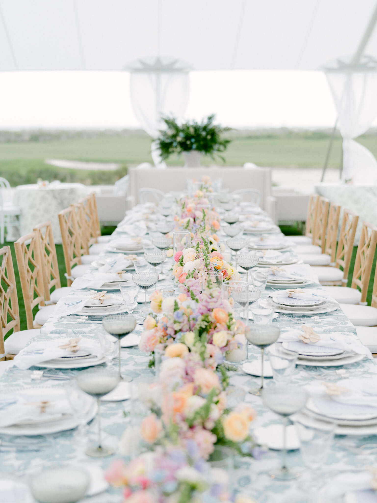 A long reception table lined with colorful pastel flowers, white plates and a blue and white floral table cloth.