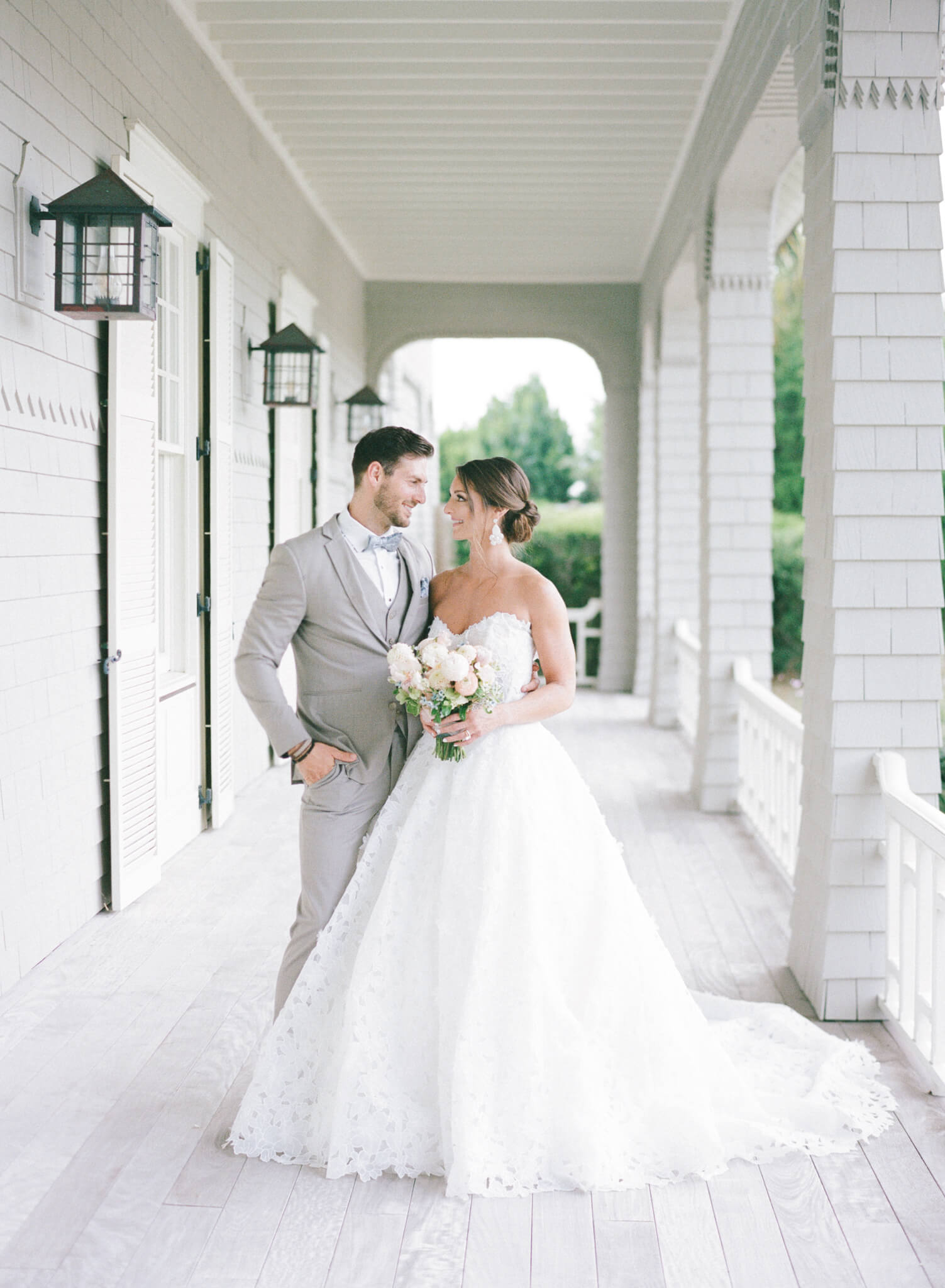 A bride in her full gown and groom in a gray suit looking at each other on the porch of the Kiawah Island Golf Course.