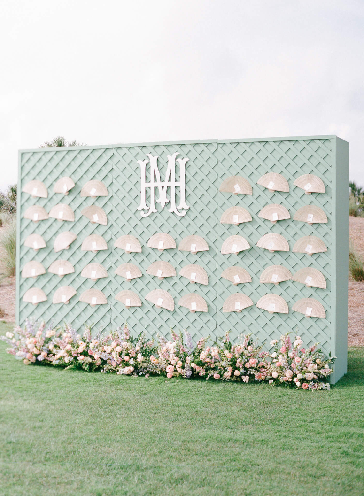 A mint escort display wall with a monogram and tan fans and flowers lining the base.