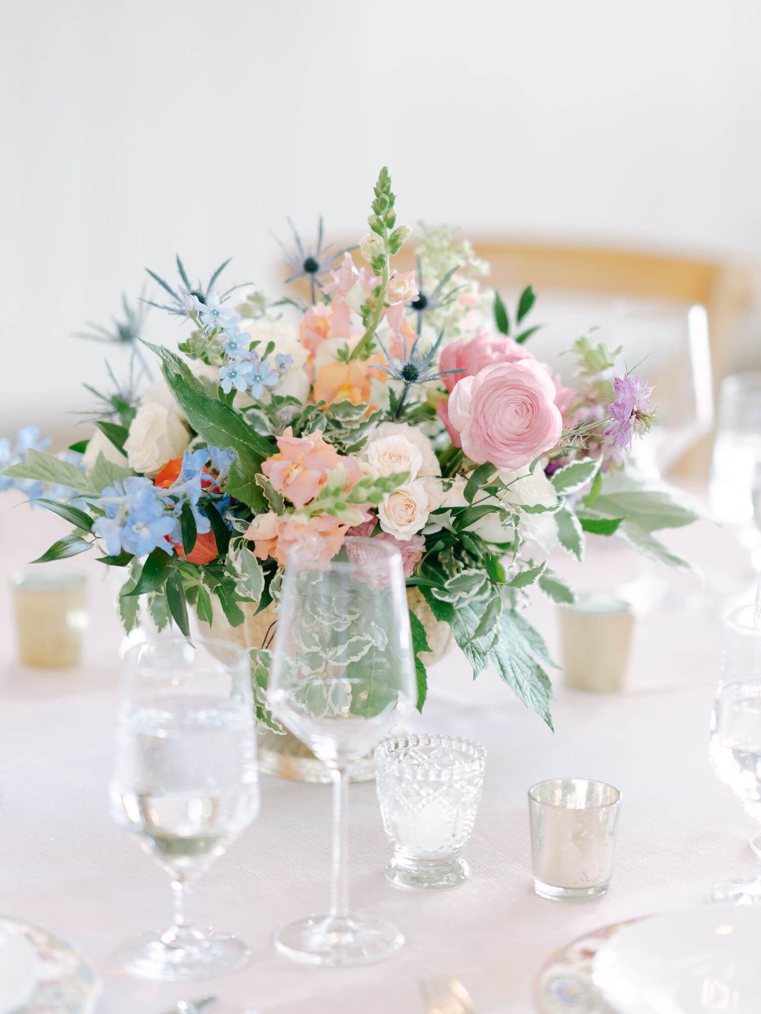 Closeup of a colorful floral centerpiece and clear glasses on a blush table cloth at a wedding reception.