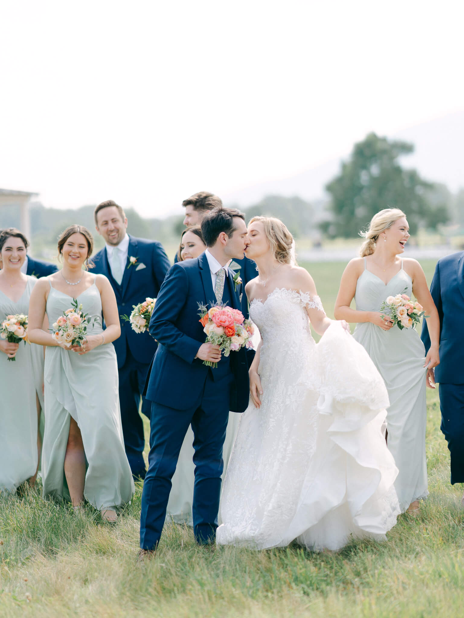 A groom and bride kissing while walking with their wedding party.