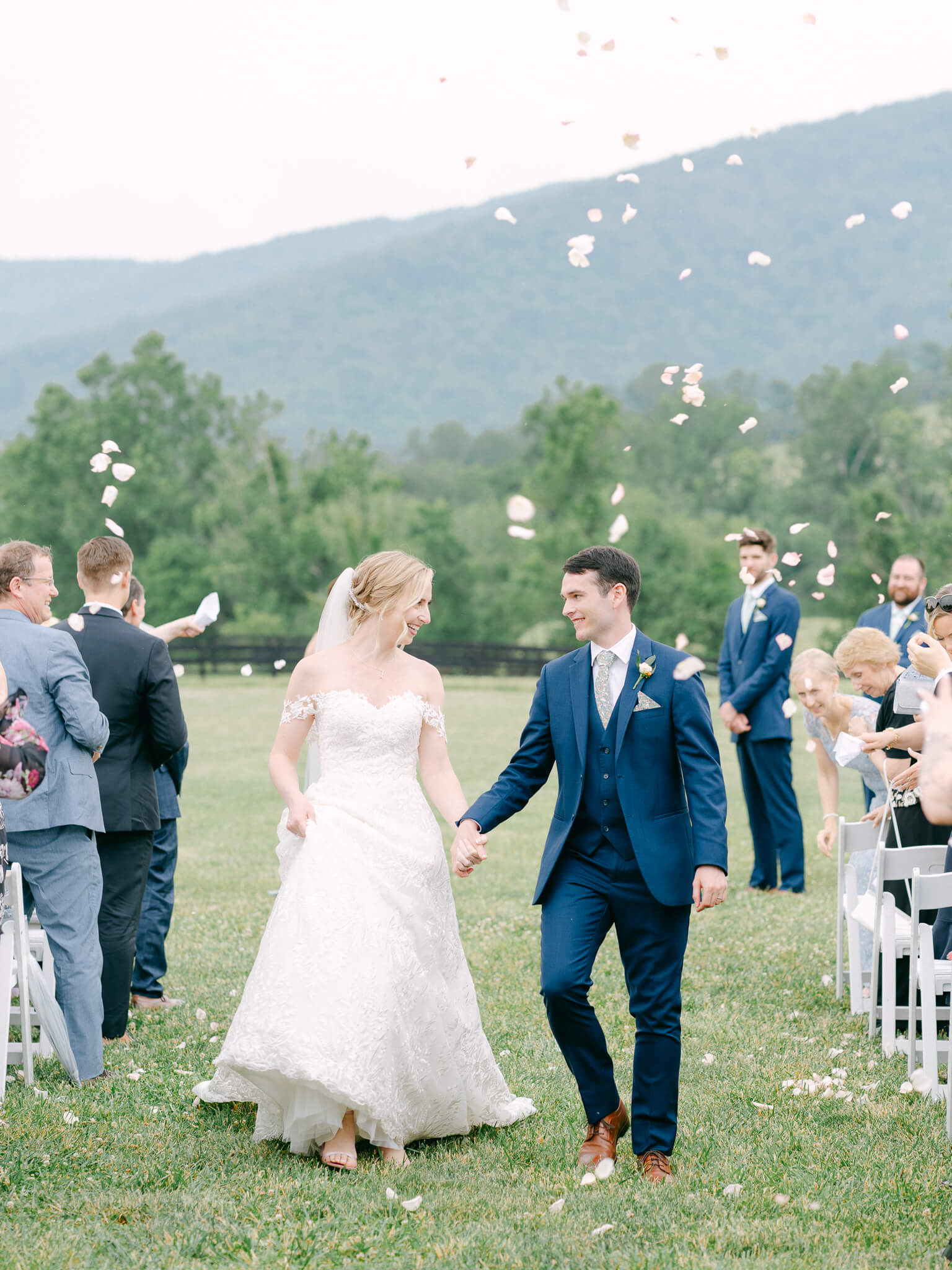The bride and groom walking down the aisle in front of Virginia's hills after being married while white petals are thrown.