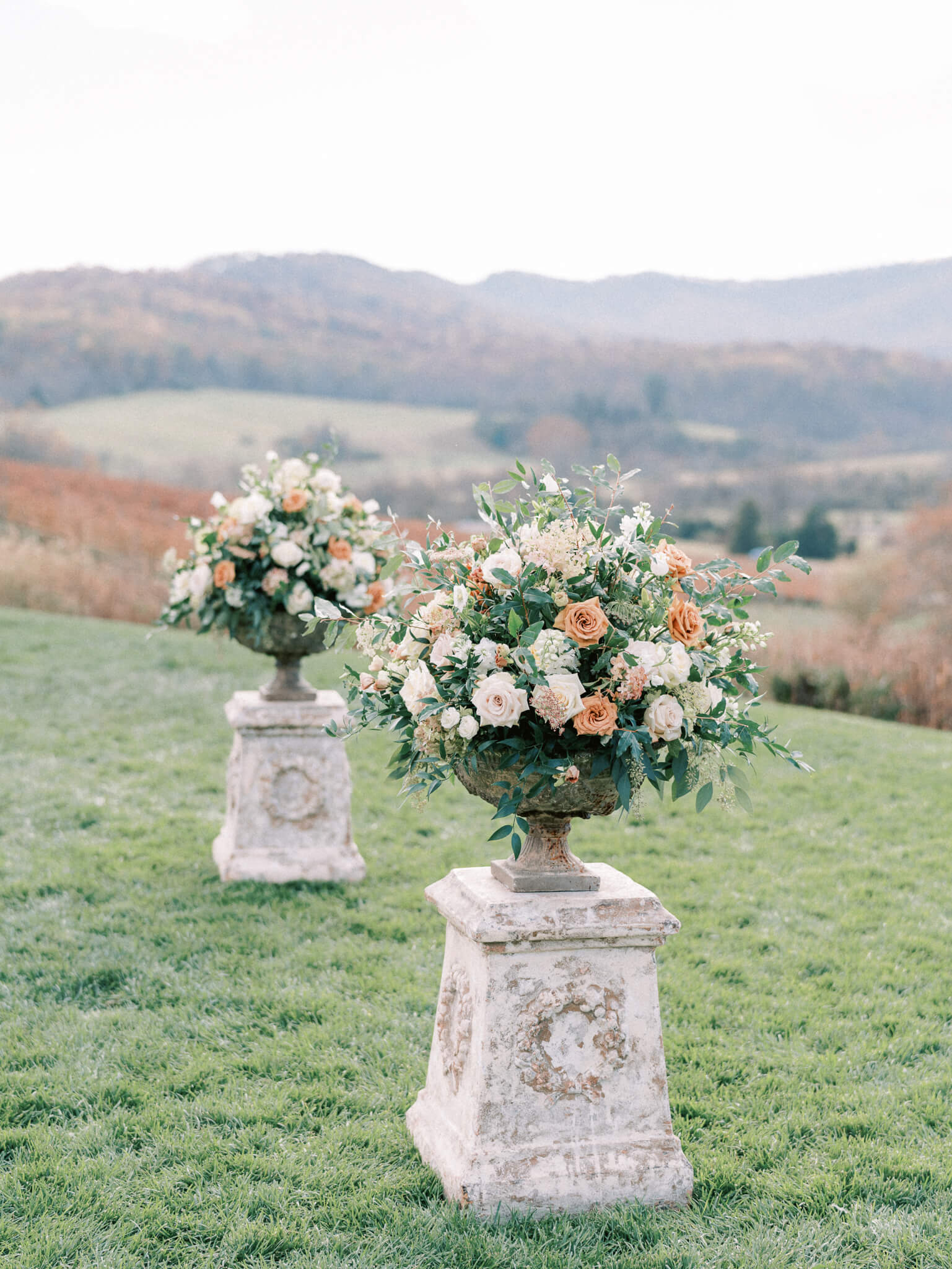 Extravagant floral ceremony pieces of peach, blush and cream roses sitting on stone pillars in front of mountain views at a Pippin Hill wedding.