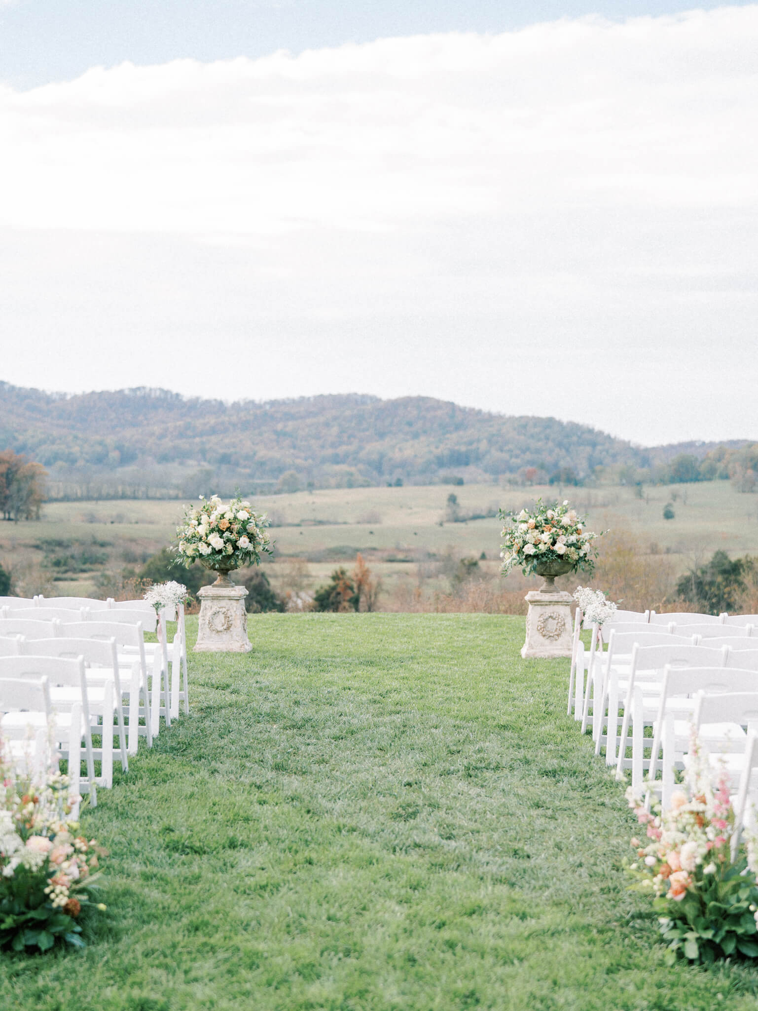 An empty ceremony set up with white wooden chairs and large floral centerpieces at a Pippin Hill wedding.