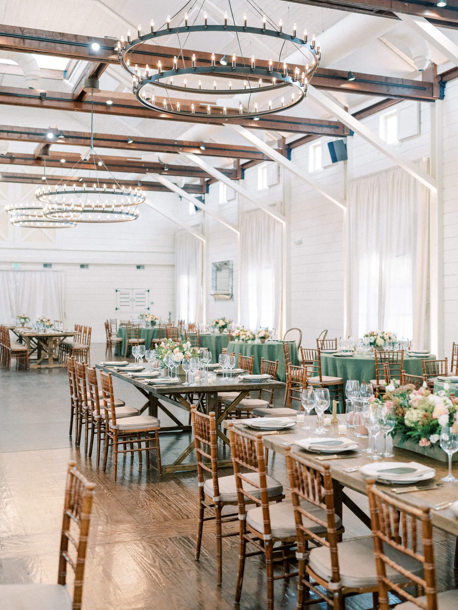 The Pippin Hill wedding reception space with wooden chairs and tables, green table cloths and peach and cream florals.