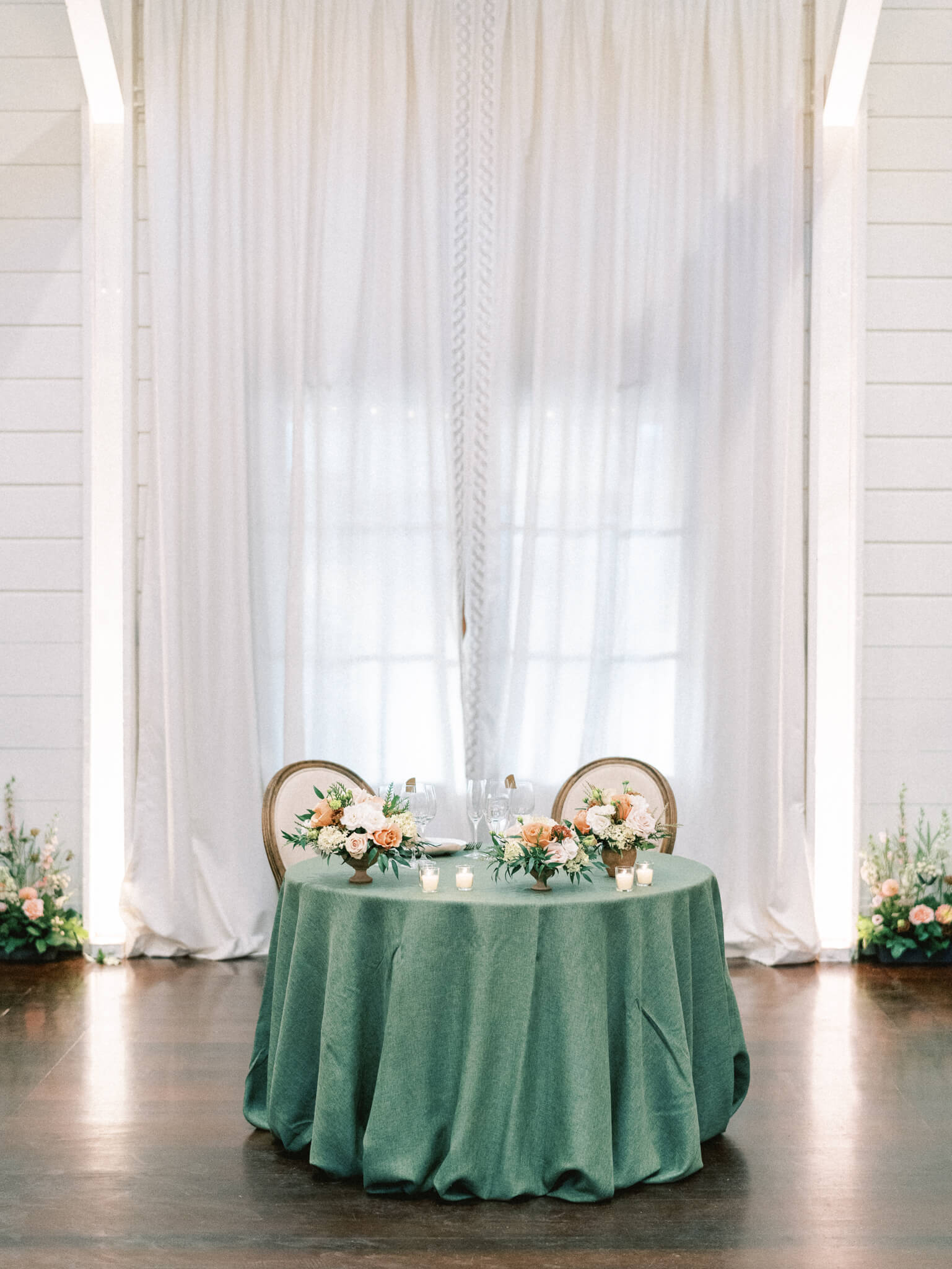 A sweetheart table at a Pippin Hill wedding reception with a green tablecloth, votive candles and peach and cream florals.