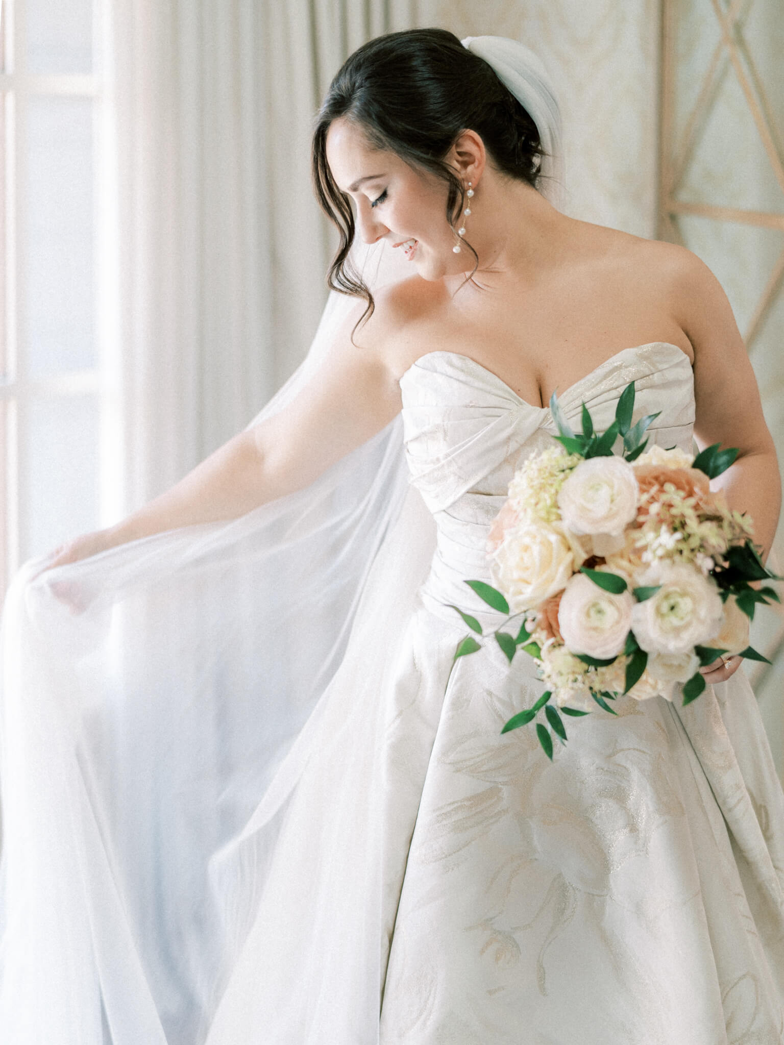 Closeup of a bride in her wedding gown holding her bouquet and playing with her veil.