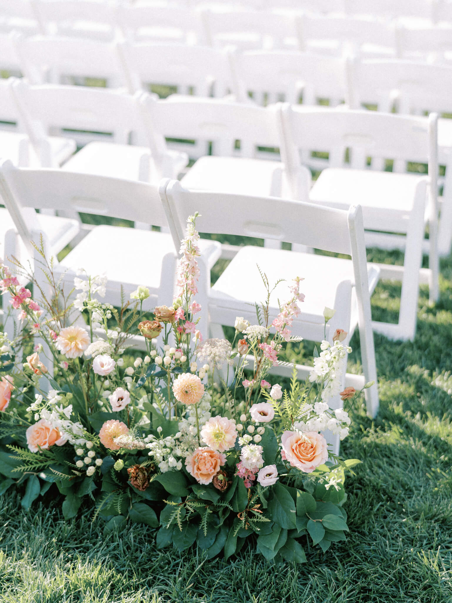 White wooden folding chairs and peach colored floral pieces at a Pippin Hill wedding ceremony.