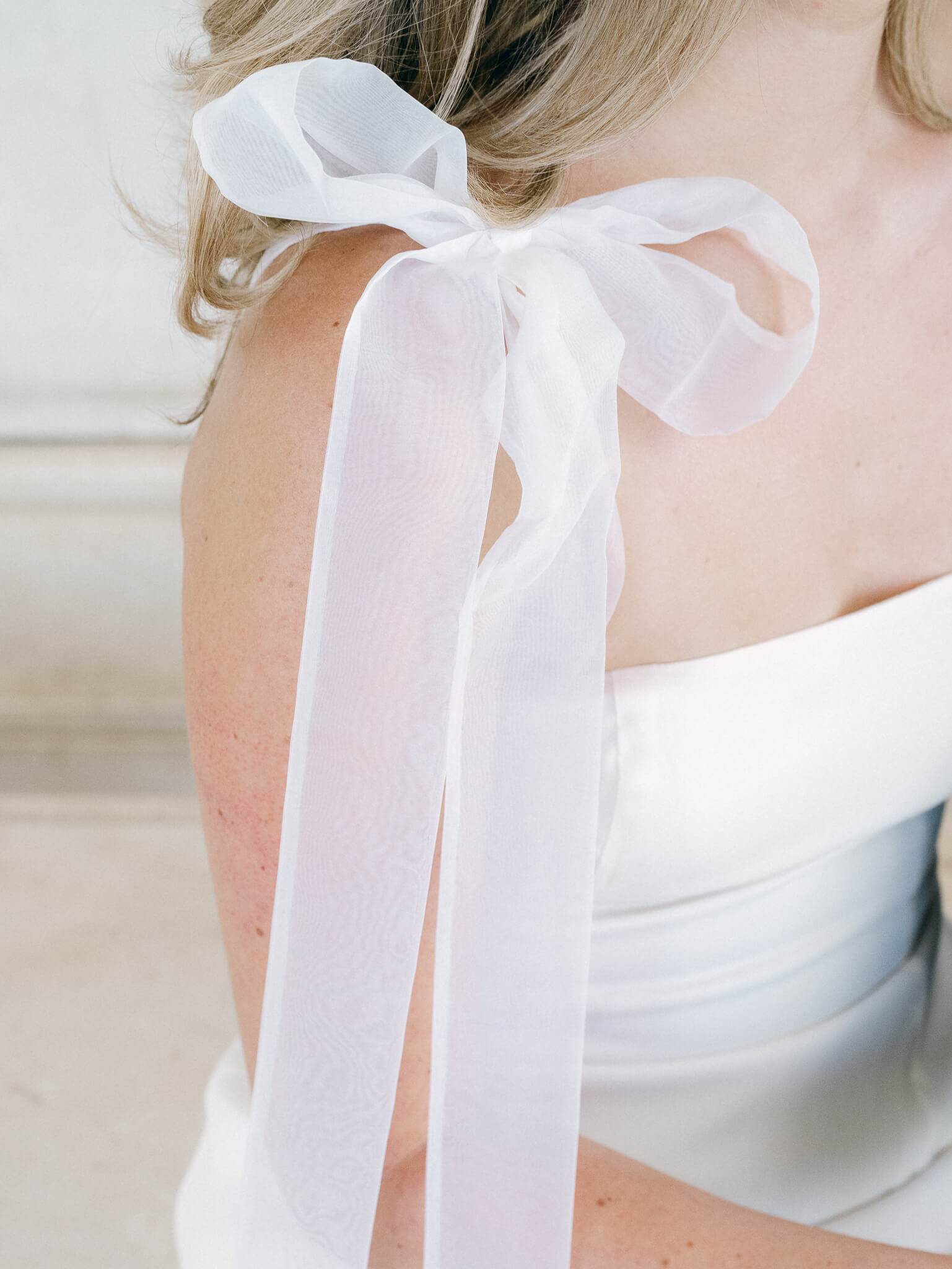 Closeup of a white tulle bow tied on the shoulder of a woman's dress.