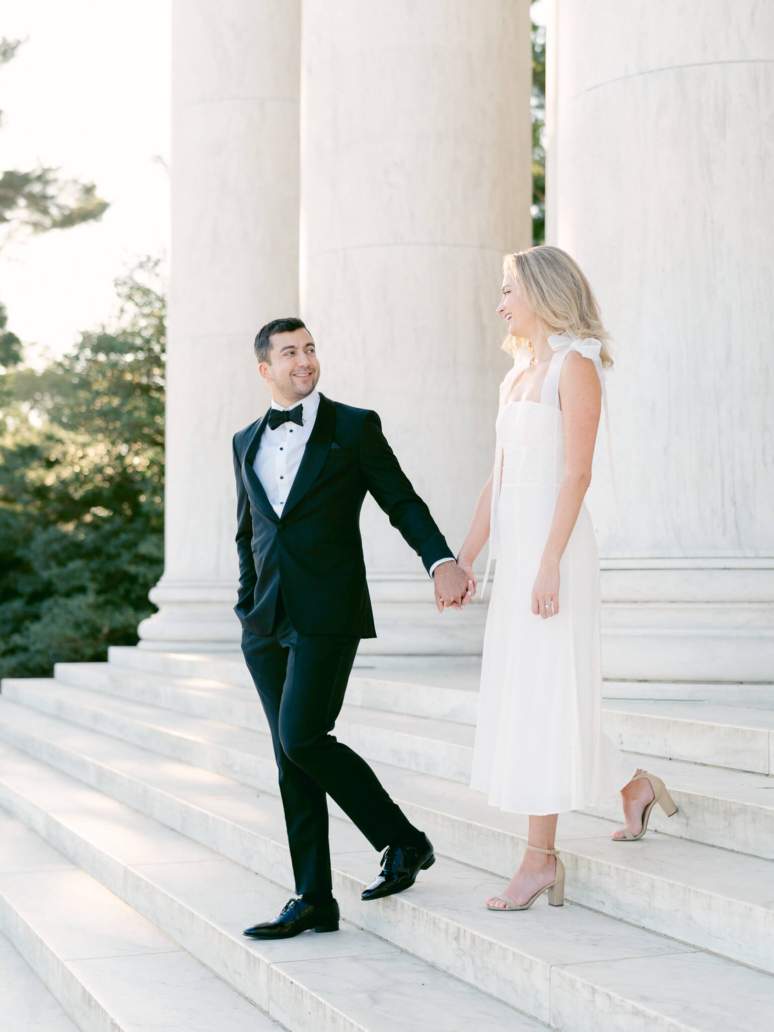 A man in a tux leading his fiancée down the steps of the Jefferson Memorial.