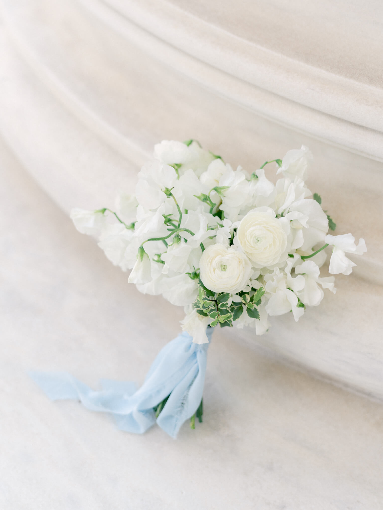 A bouquet of white ranunculus and sweet peas tied with a blue ribbon.