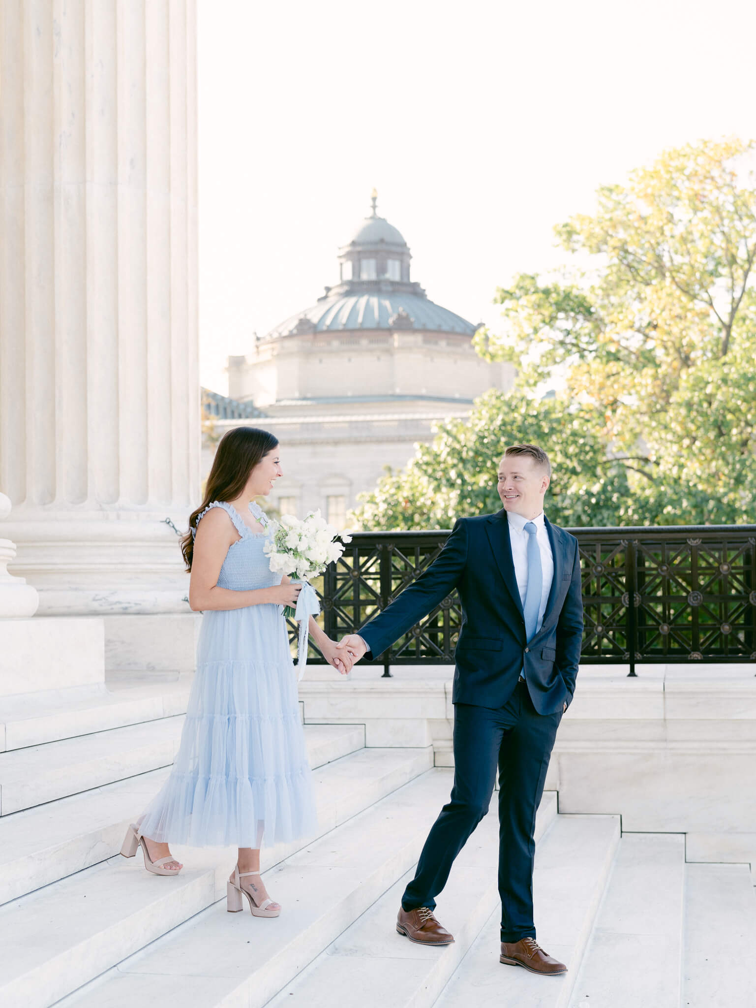 A man and woman holding hands walking down the steps of the Supreme Court.