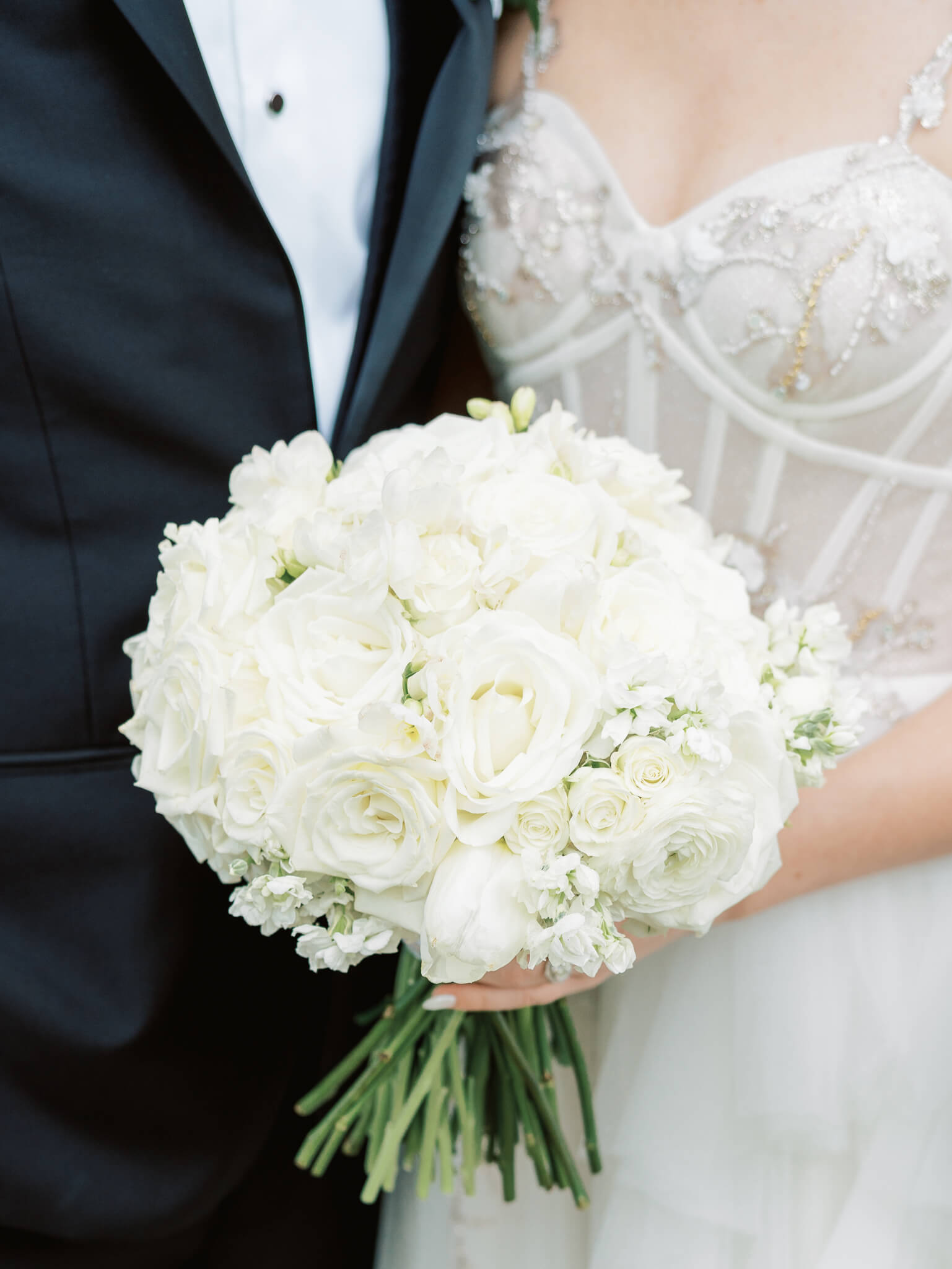Closeup of a bride and groom standing together and holding a bouquet of white flowers