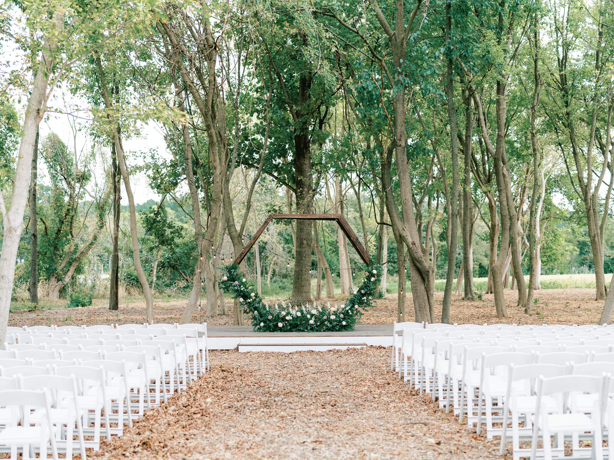 Ceremony space with white chairs and floral arbor nestled amongst the trees at Kent Island Resort