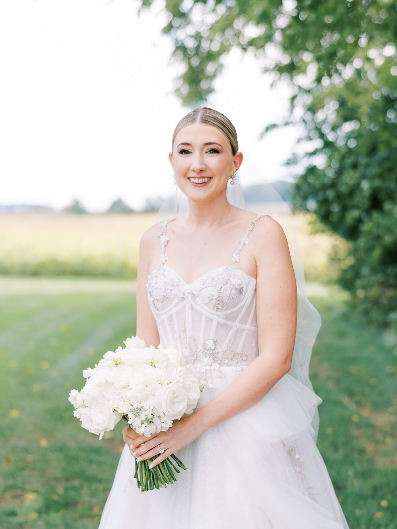 Closeup of a bride on her wedding day holding her bouquet standing in front of a field and shrubs