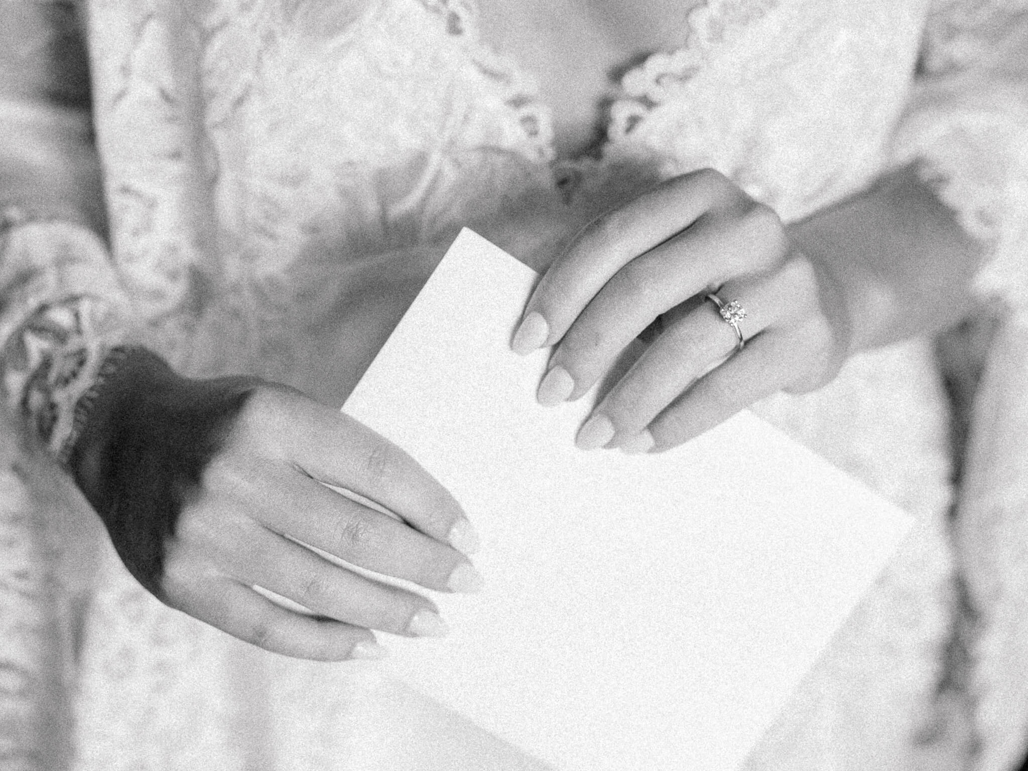 Close-up of a bride's hands holding an envelope and showing off her engagement ring.