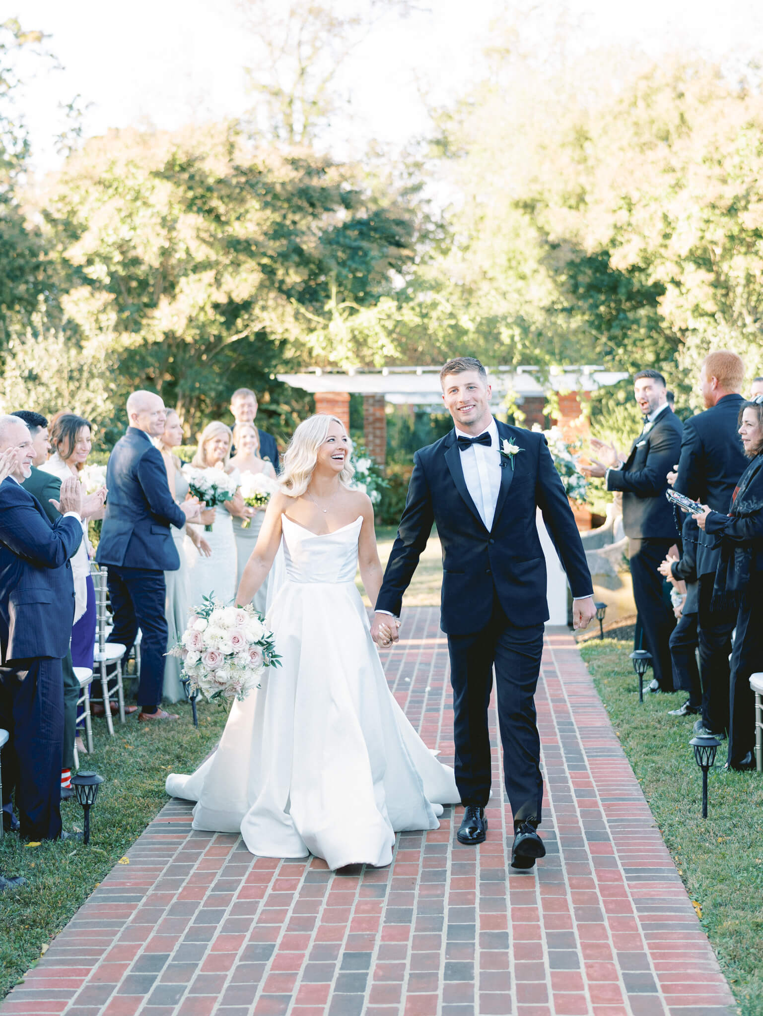 A bride and groom walking down the aisle smiling after getting married while their guests are standing and cheering.
