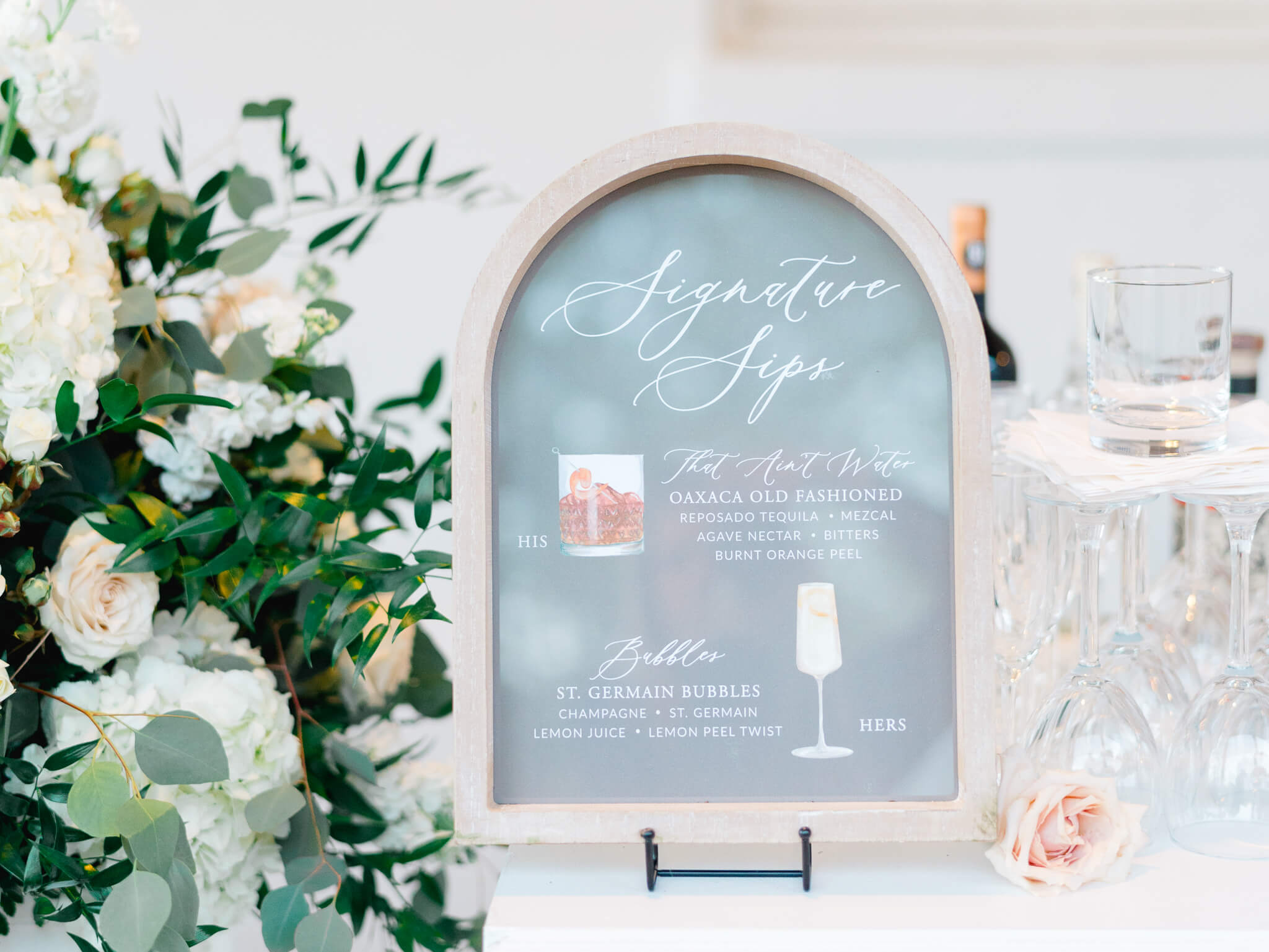 Signature drink sign and a floral centerpiece sitting on the bar at River Farm Wedding Venue in Alexandria, Virginia.