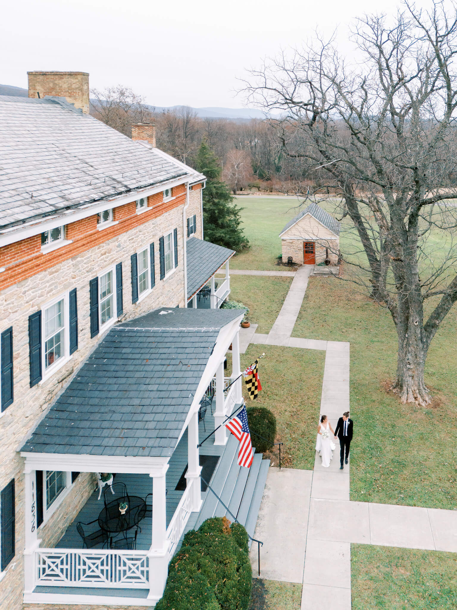 Aerial view of a bride and groom walking hand in hand at Springfield Manor's historic house.