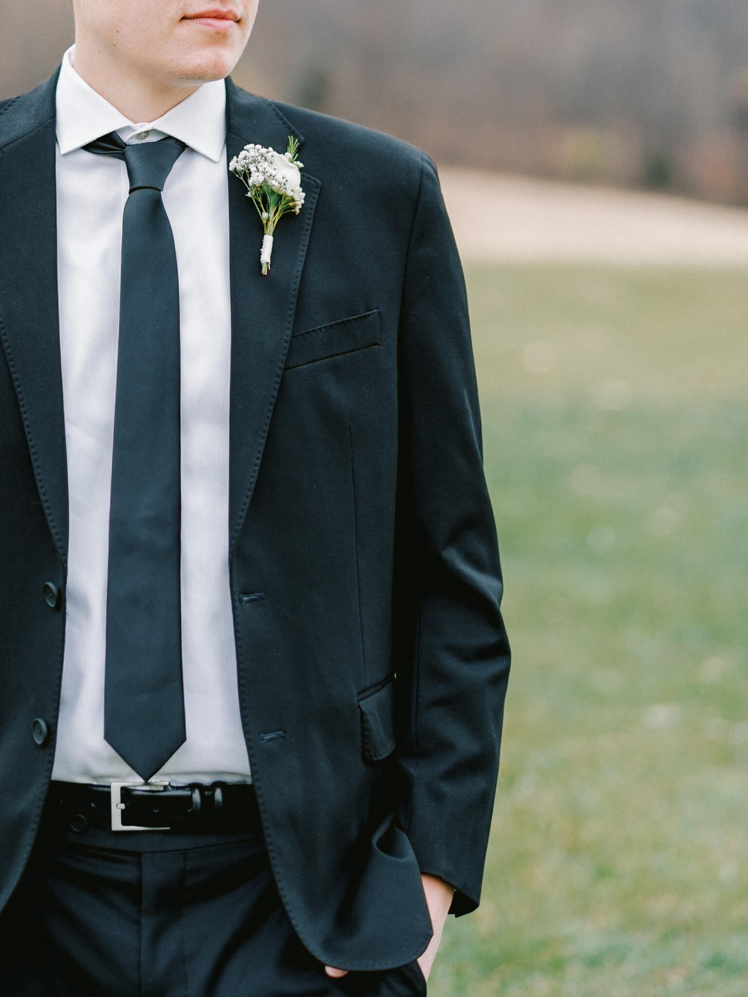 Close-up of a groom's black suit and tie and his white boutonnière.