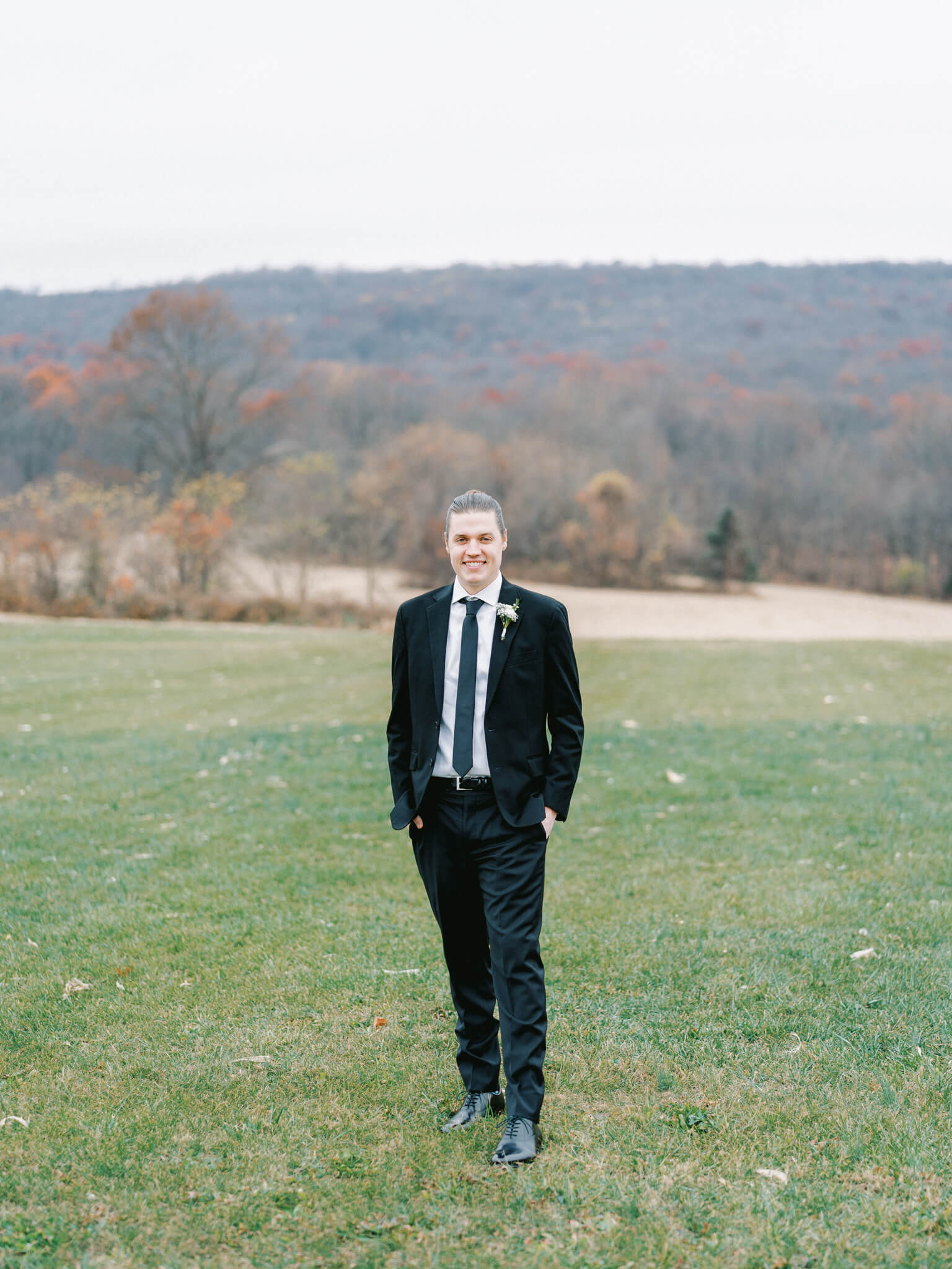 Full length portrait of a groom in a black suit in front of the mountainous backdrop at Springfield Manor wedding venue.