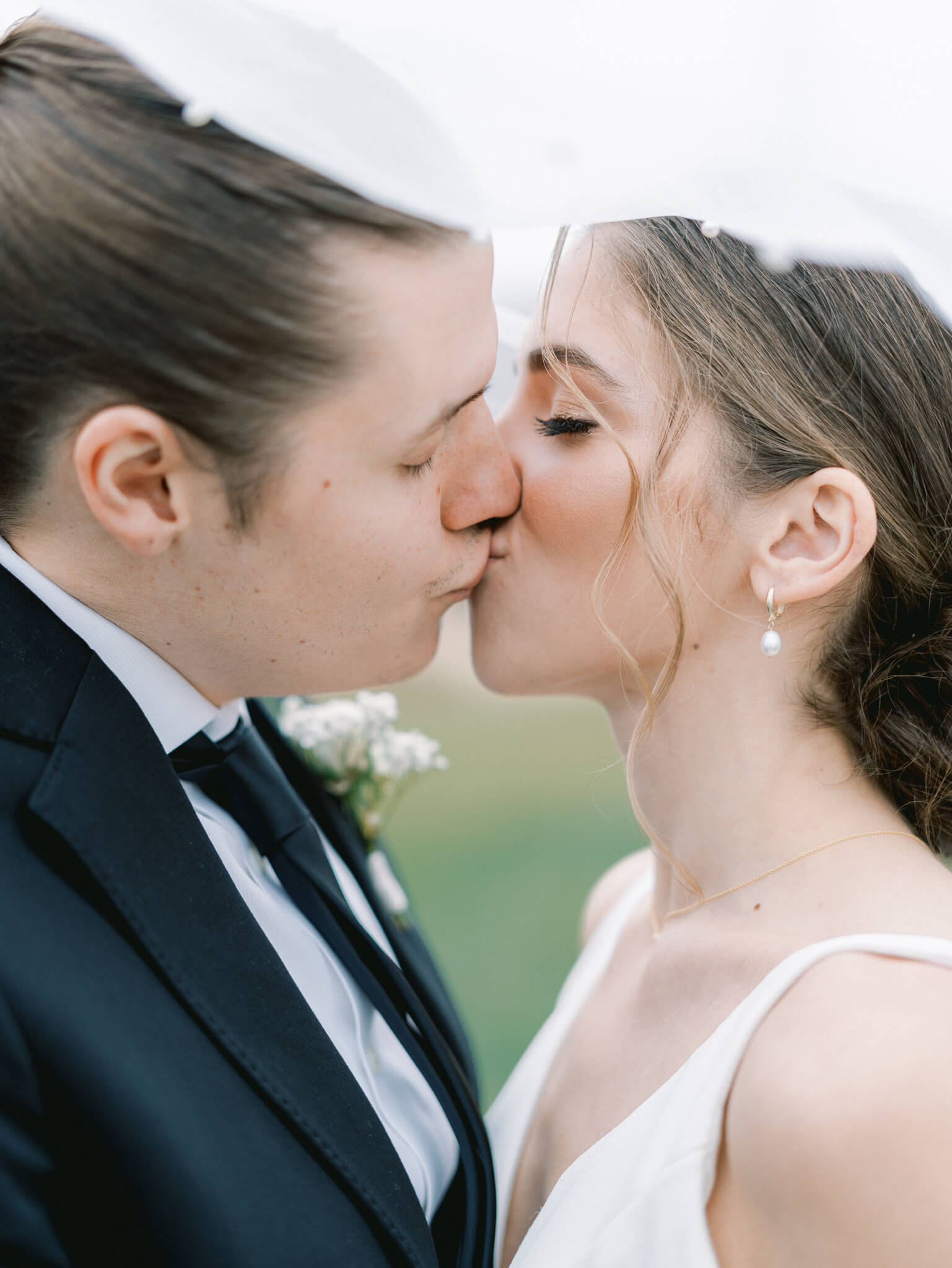 Close-up of a bride and groom kissing under a veil.