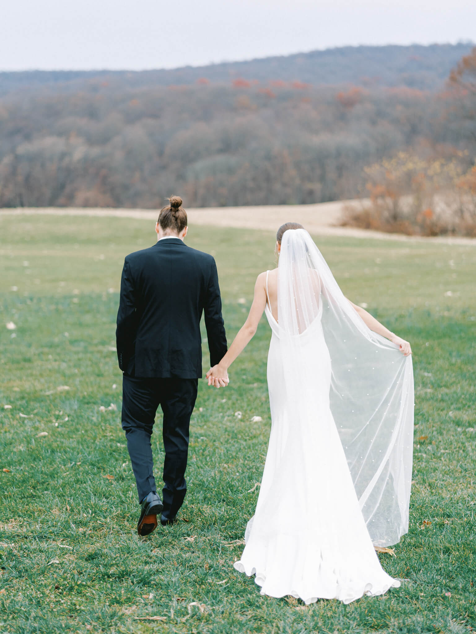 A bride and groom holding hands and walking away towards the mountainous backdrop.