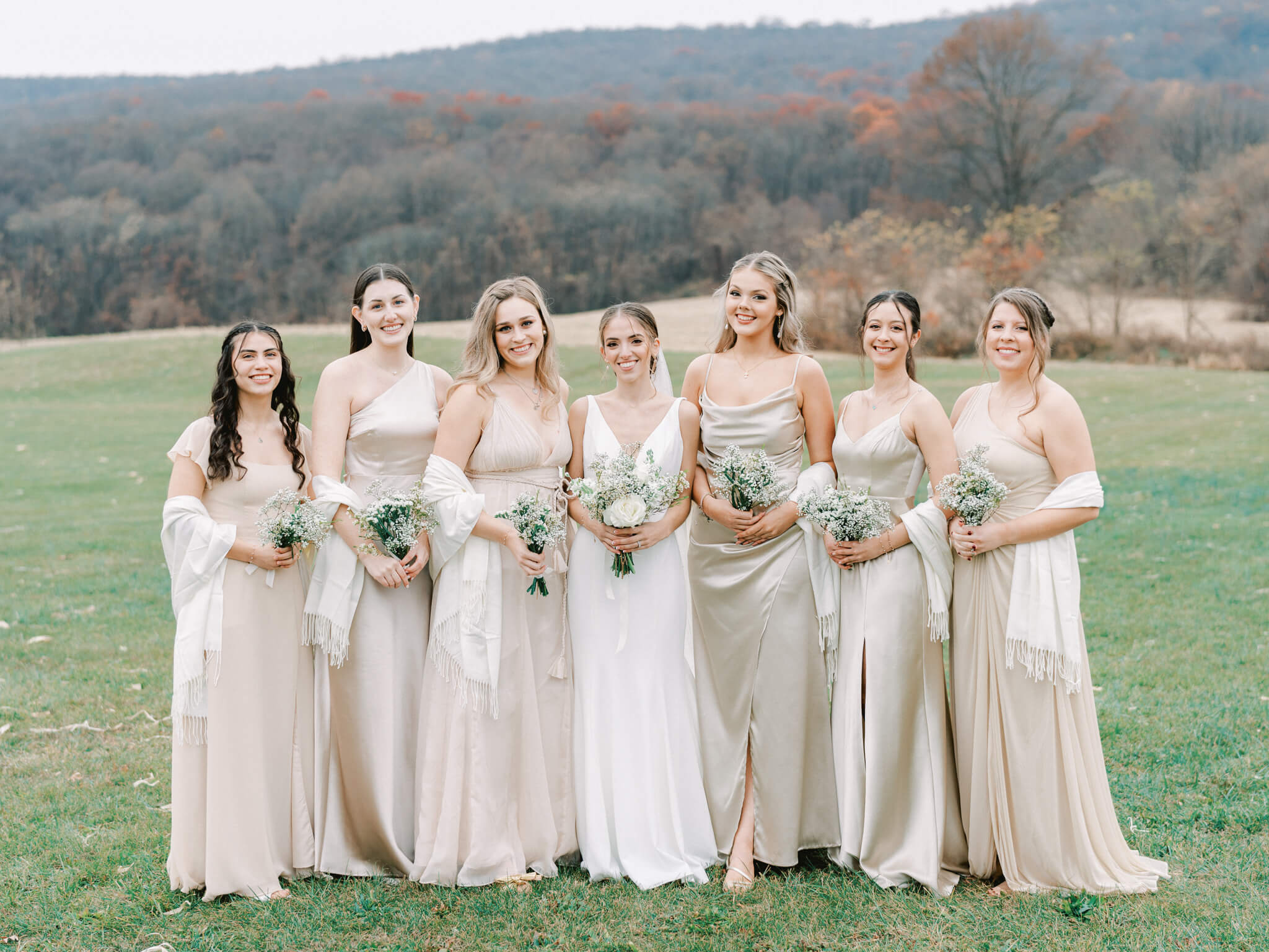 A bride and her bridesmaids in champagne satin dresses in front of a mountainous backdrop.