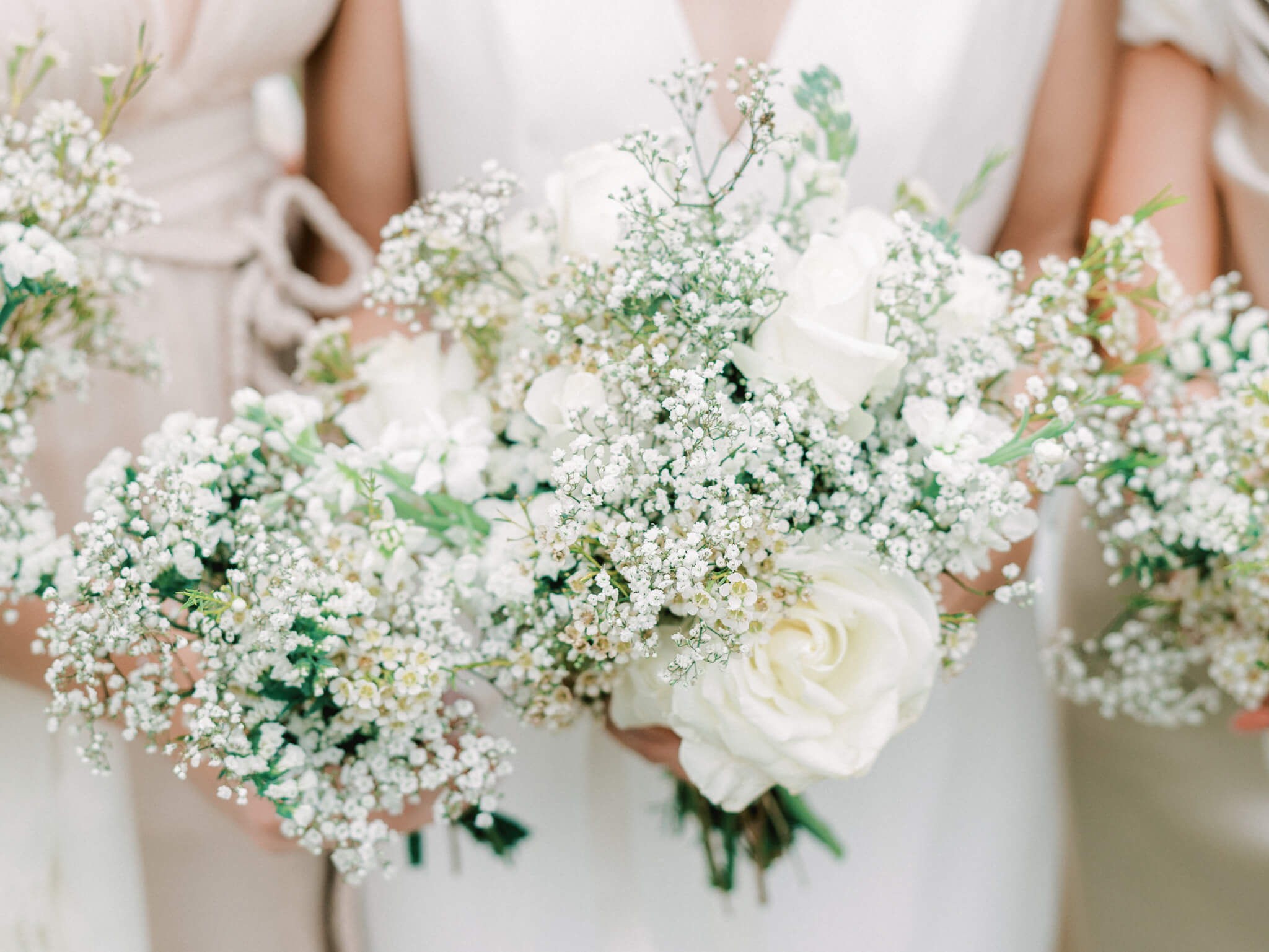 Close-up of the bouquets a bride and her bridesmaids are holding made of white roses and baby's breath.
