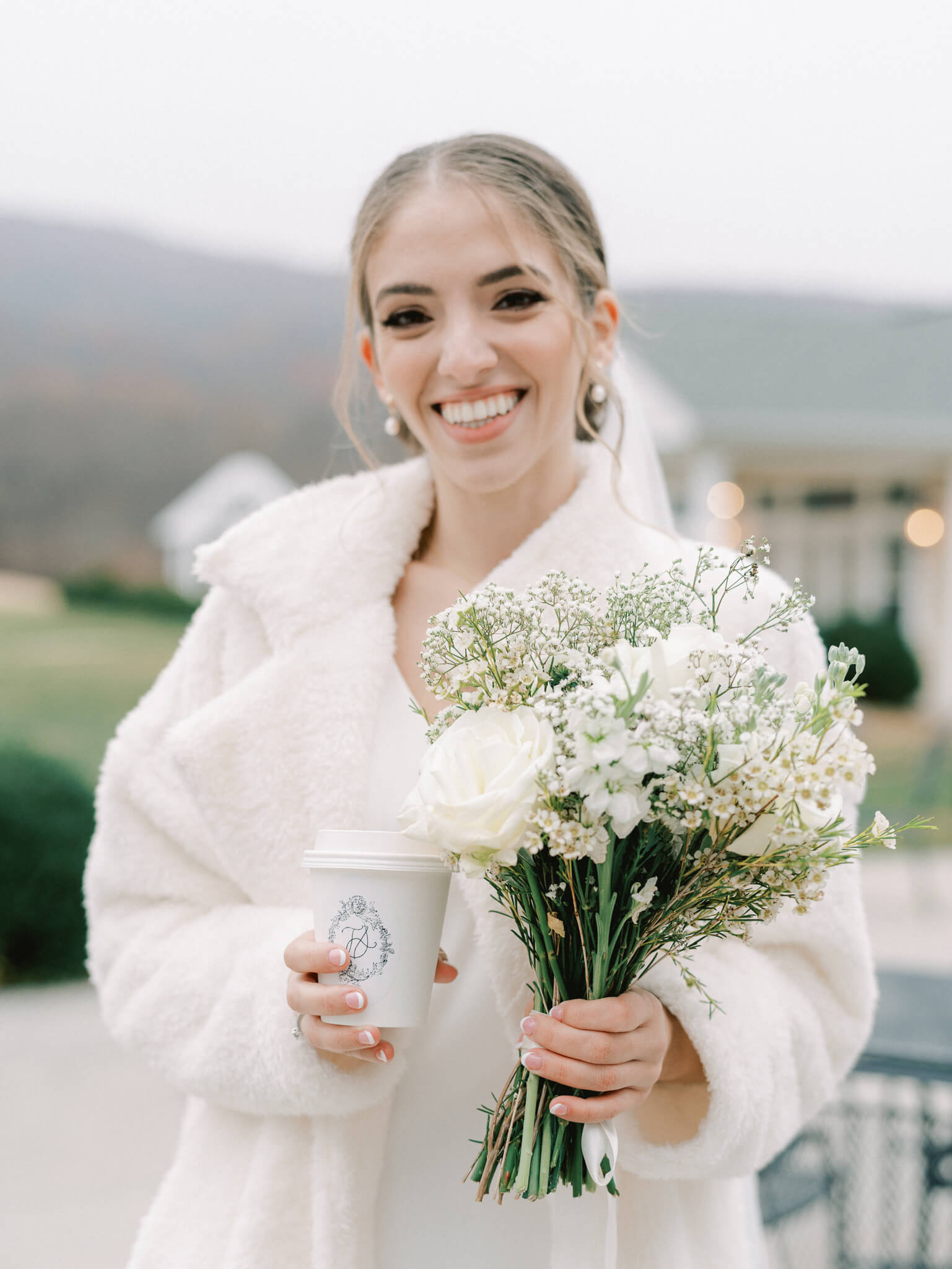 Close-up of a bride holding her bouquet in one hand and her monogrammed paper coffee in the other.