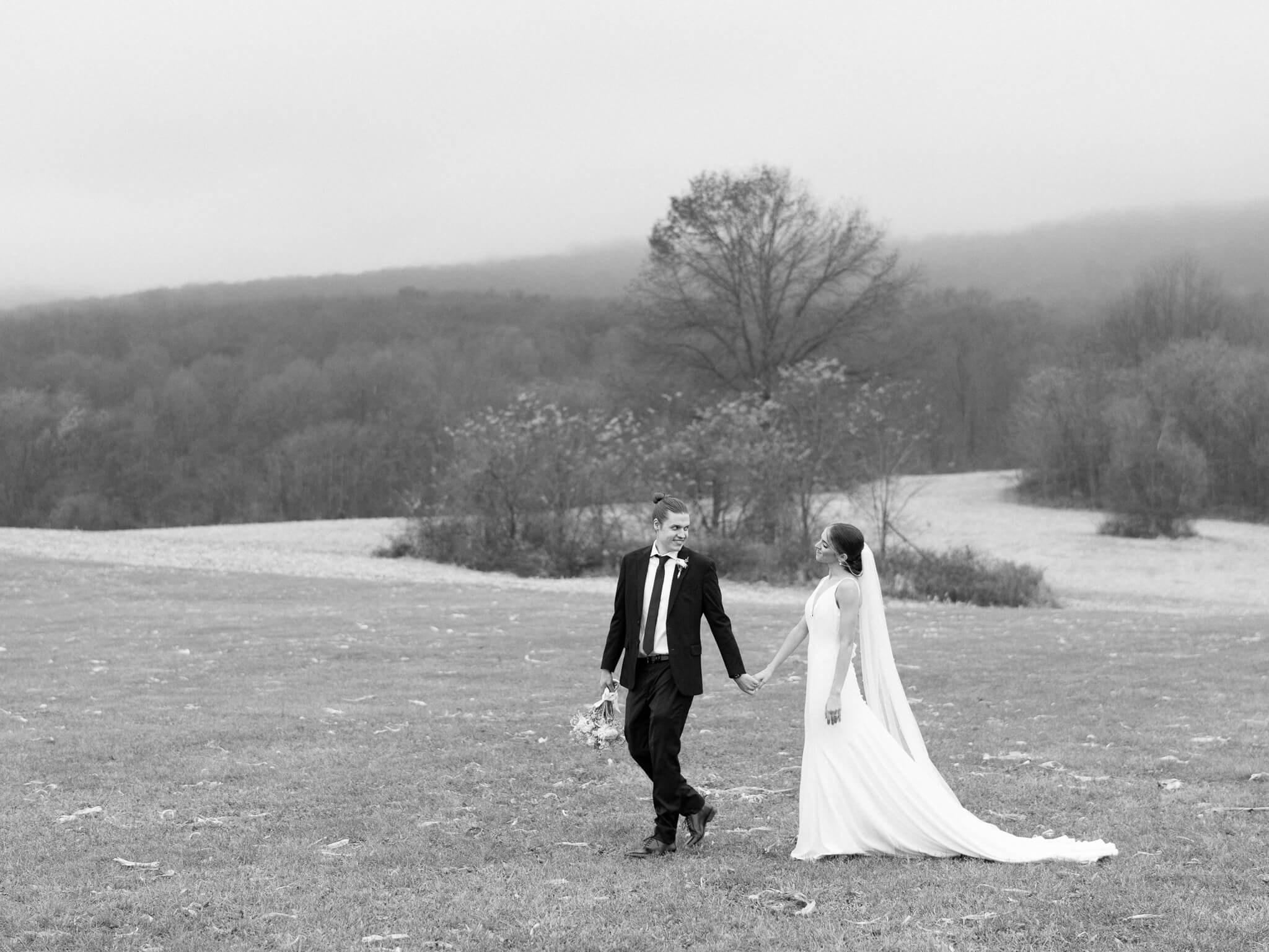 A black and white of a groom leading his bride along the foggy mountainous backdrop of Springfield Manor wedding venue.