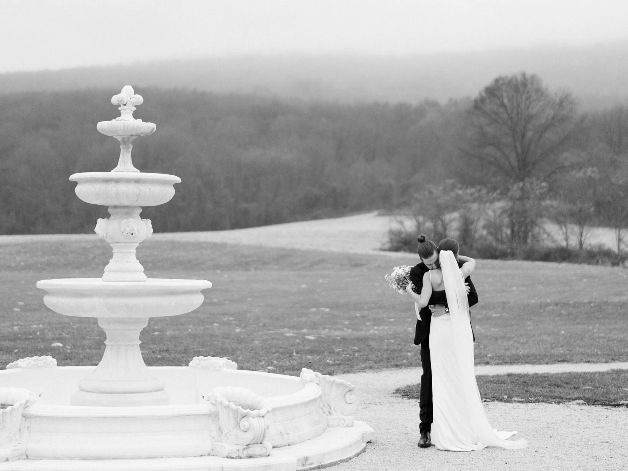 A black and white image of a groom and bride embracing on their foggy wedding day next to Springfield Manor's fountain.