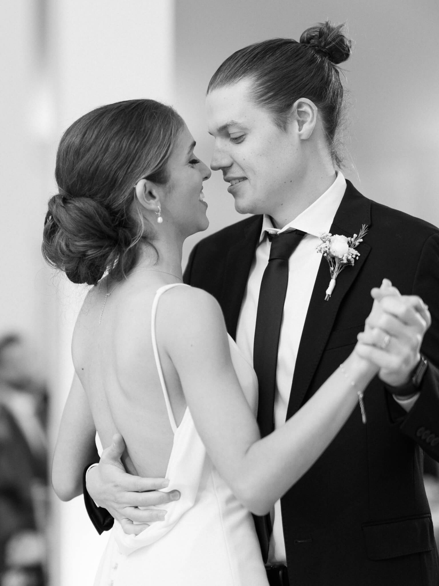 Close-up black and white image of a bride and groom smiling at each other during their first dance.
